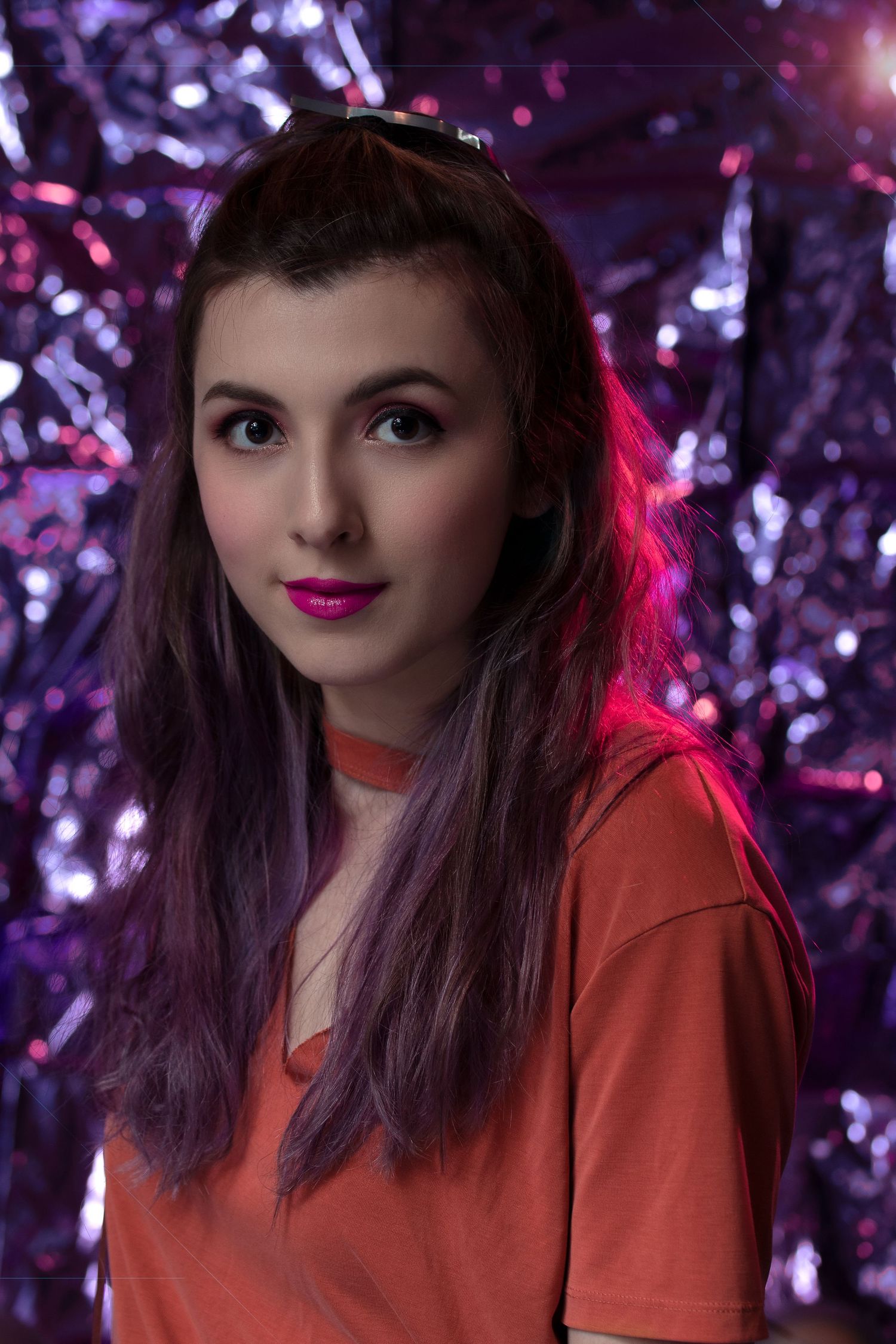 Portrait against purple sparkly backdrop with red lighting and orange jacket.