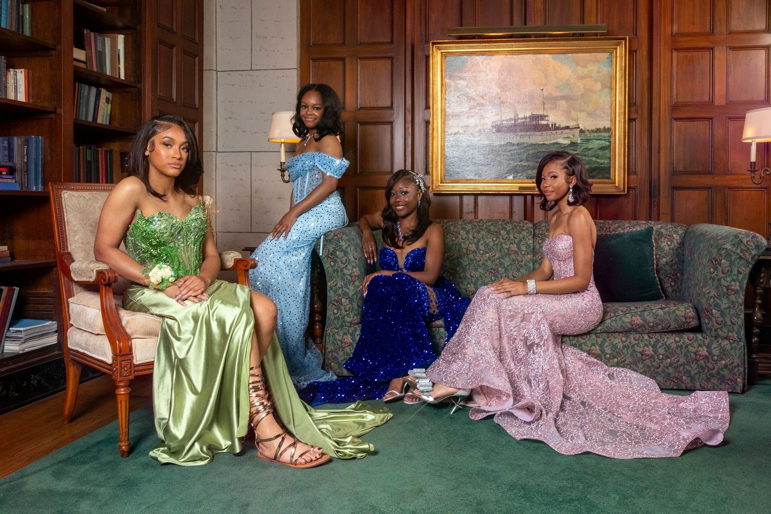 People in colorful formal gowns lounging on green carpet during an elegant photo shoot.