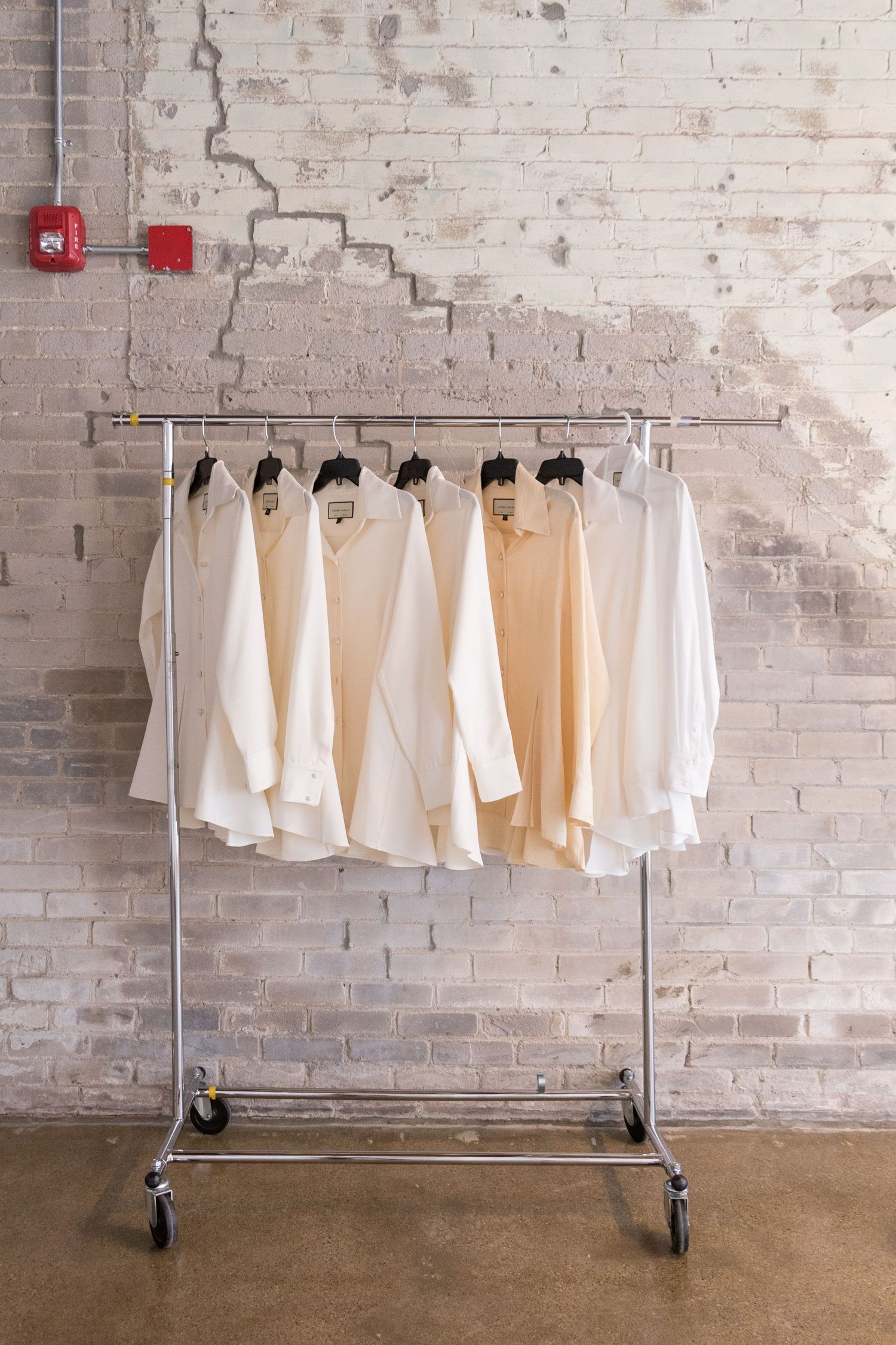 Clothing rack displaying white and cream colored garments against distressed brick wall.
