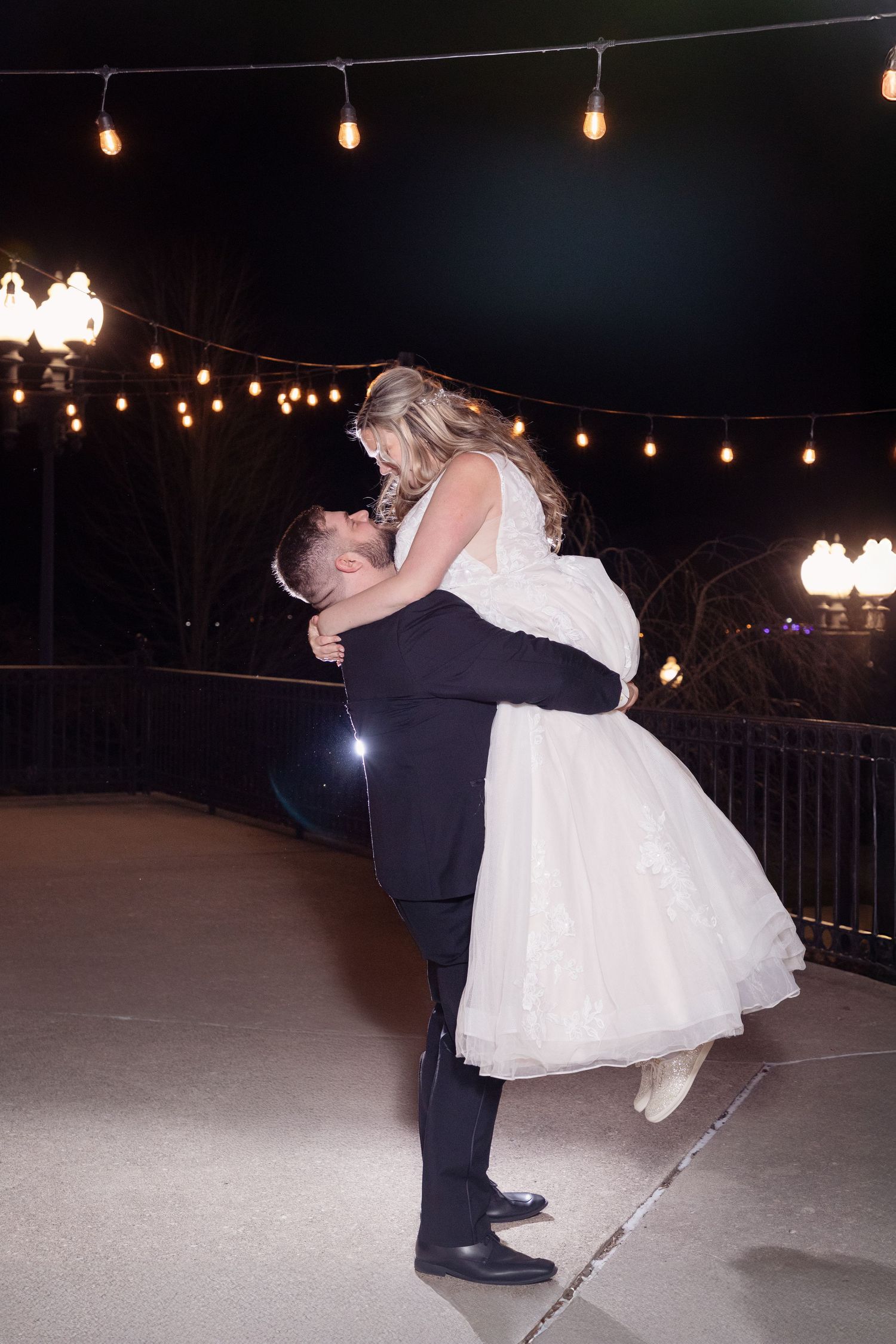 Couple shares romantic dance moment under string lights at outdoor nighttime wedding reception.