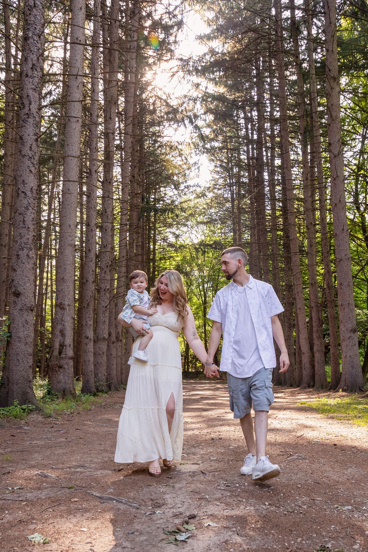 A family walking together on a pine tree-lined path during a summer photoshoot.