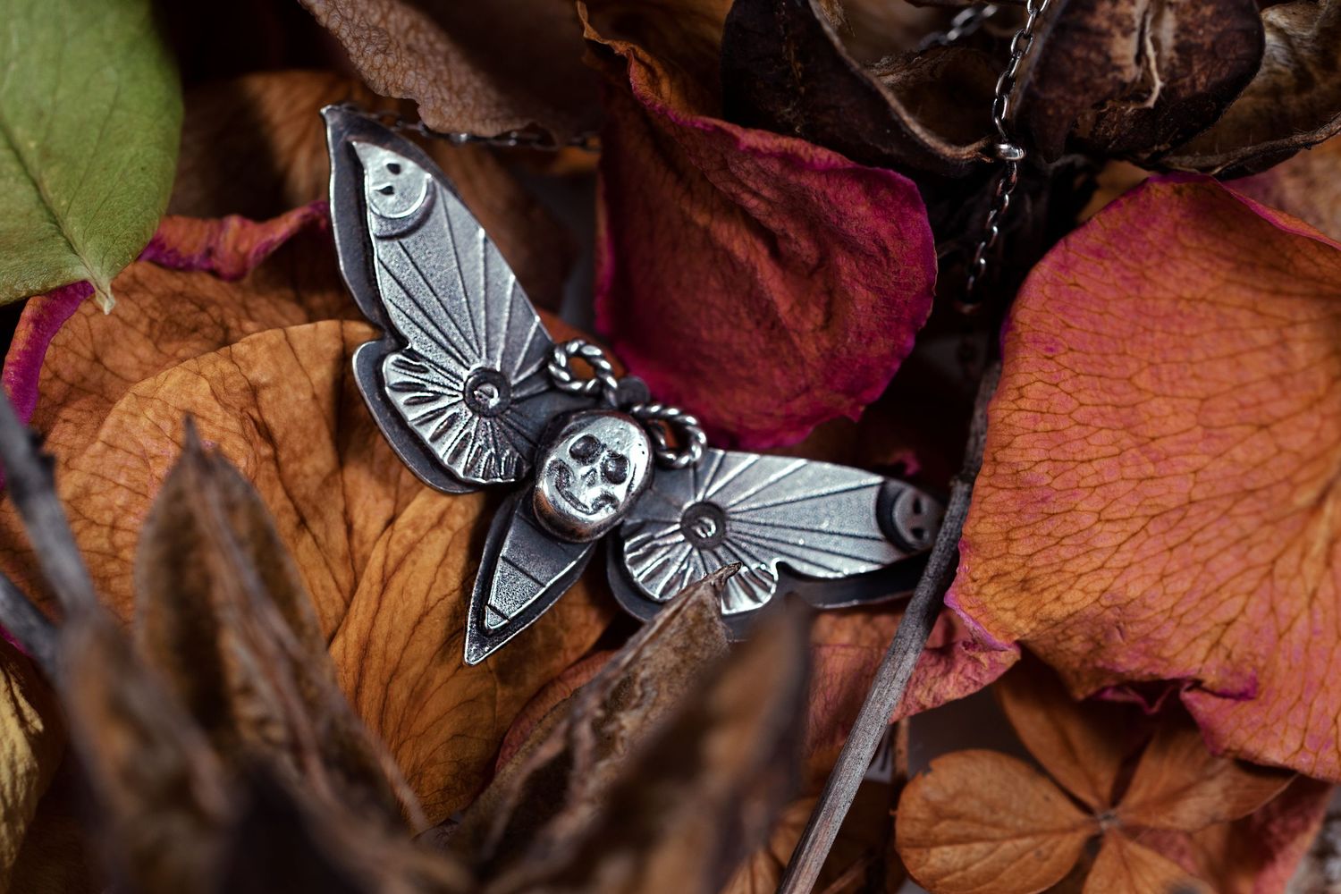 Vintage silver moth or butterfly jewelry pieces displayed on autumn leaves.