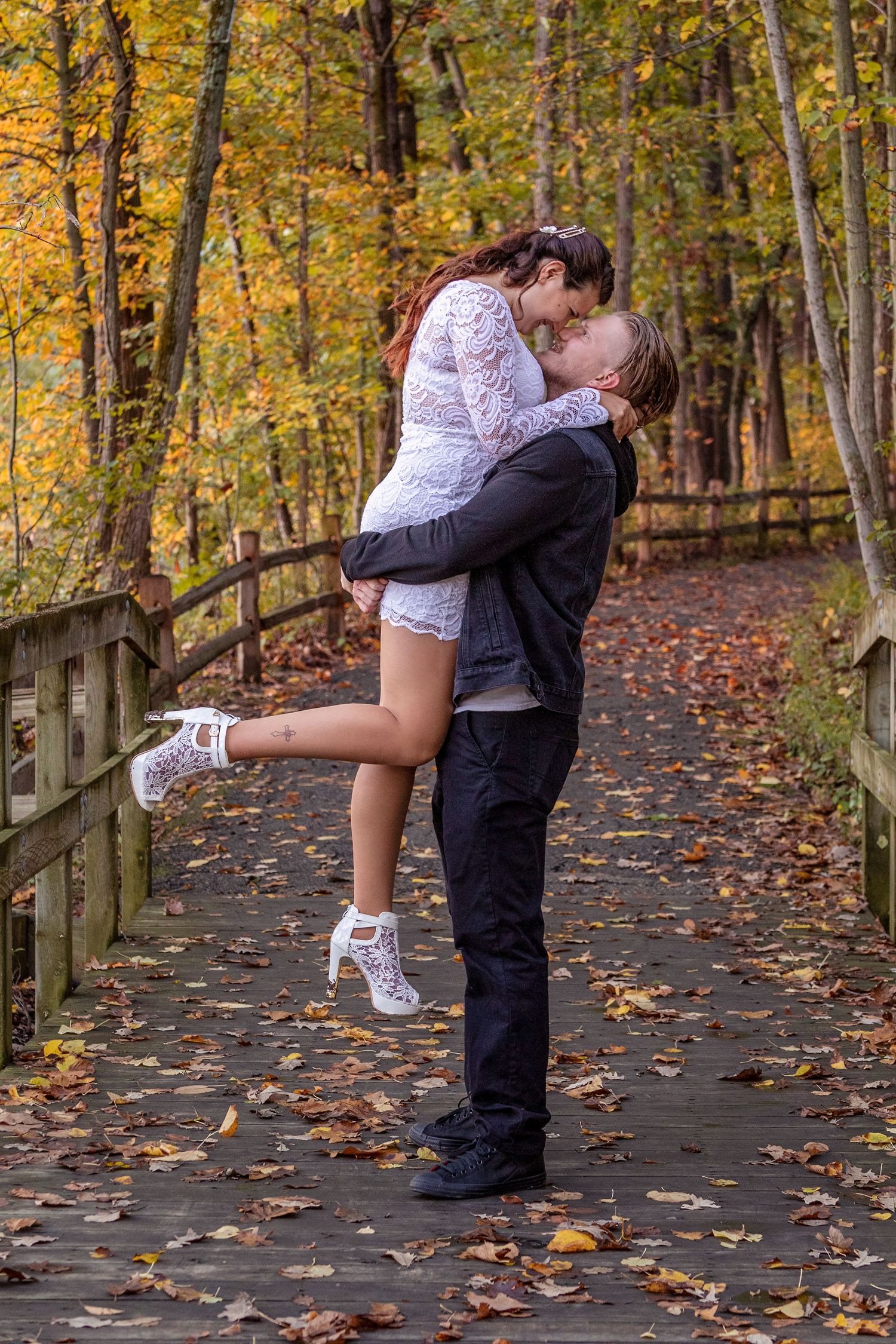 Romantic autumn engagement photos on wooden boardwalk surrounded by fall foliage.