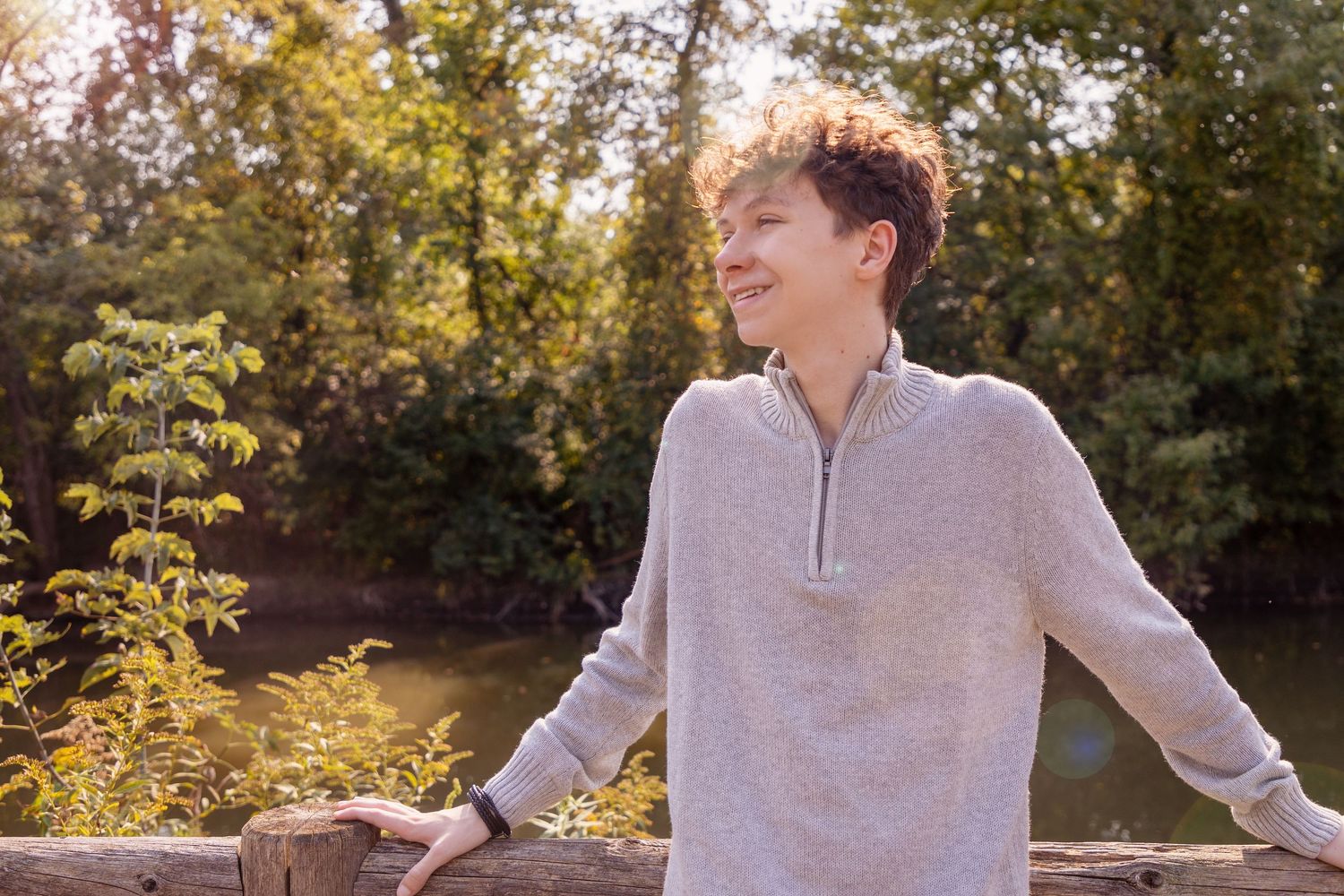 Person in beige sweater poses outdoors against autumn foliage in natural lighting.
