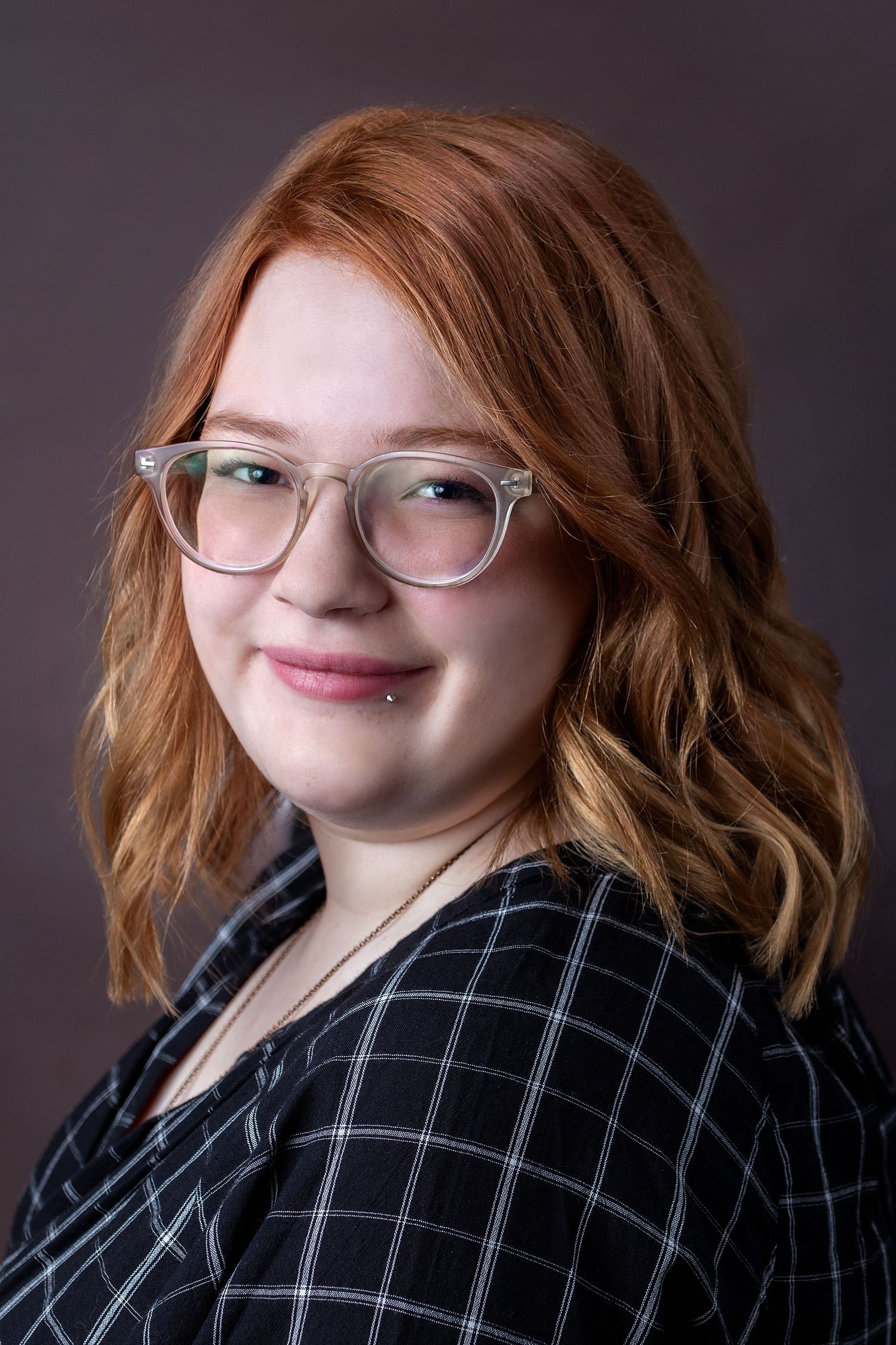Professional headshots featuring plaid blazer and glasses against dark background.