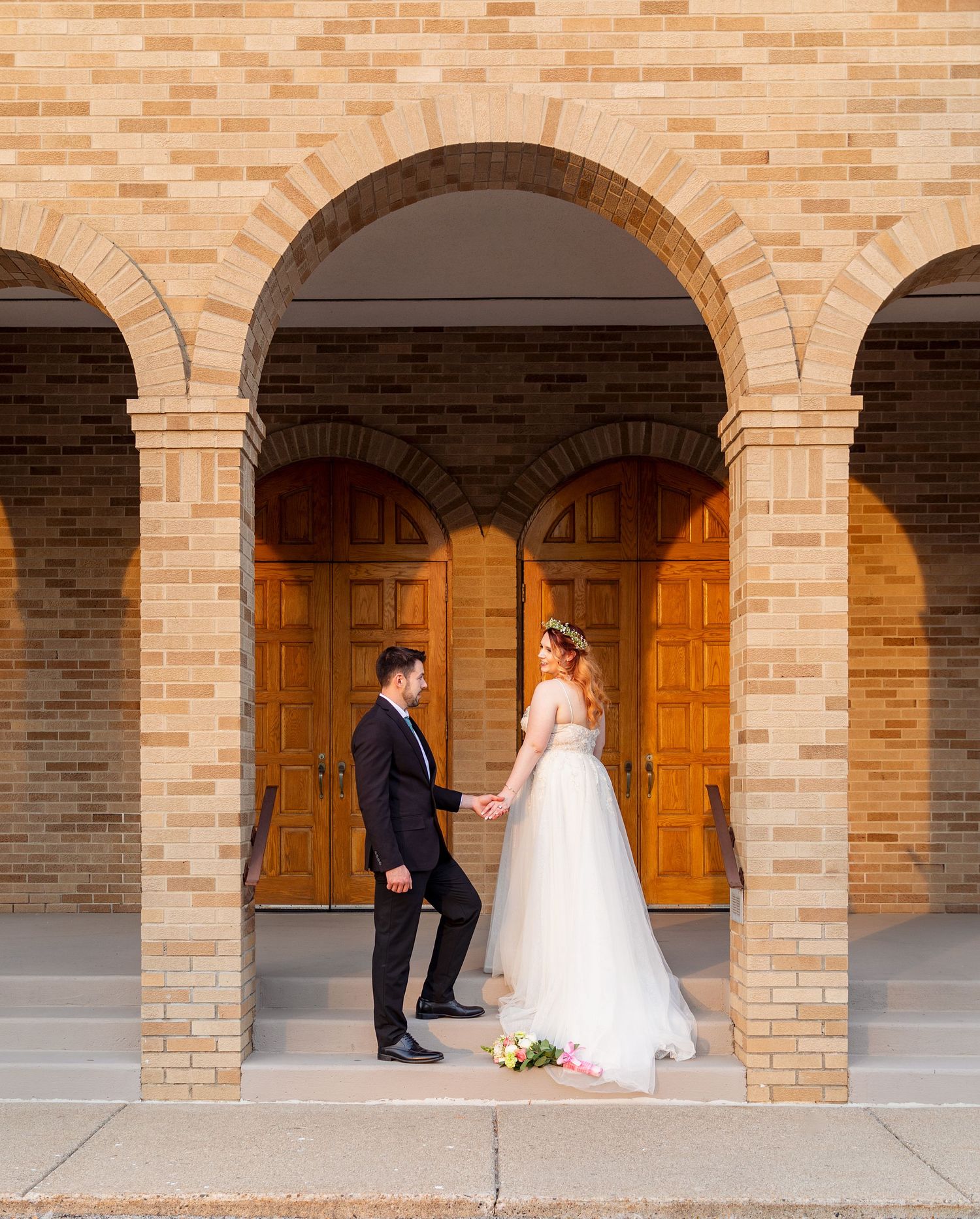 Newlyweds pose under brick archways for wedding portraits with warm wooden doors in background.