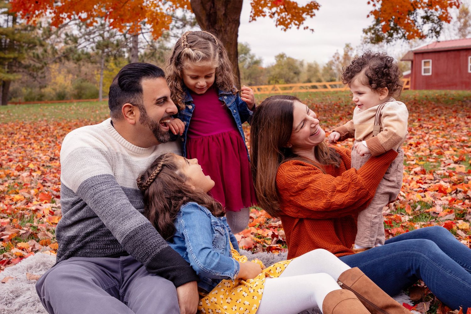 Family enjoying autumn fun while playing in vibrant red and orange fallen leaves during a fall photoshoot.