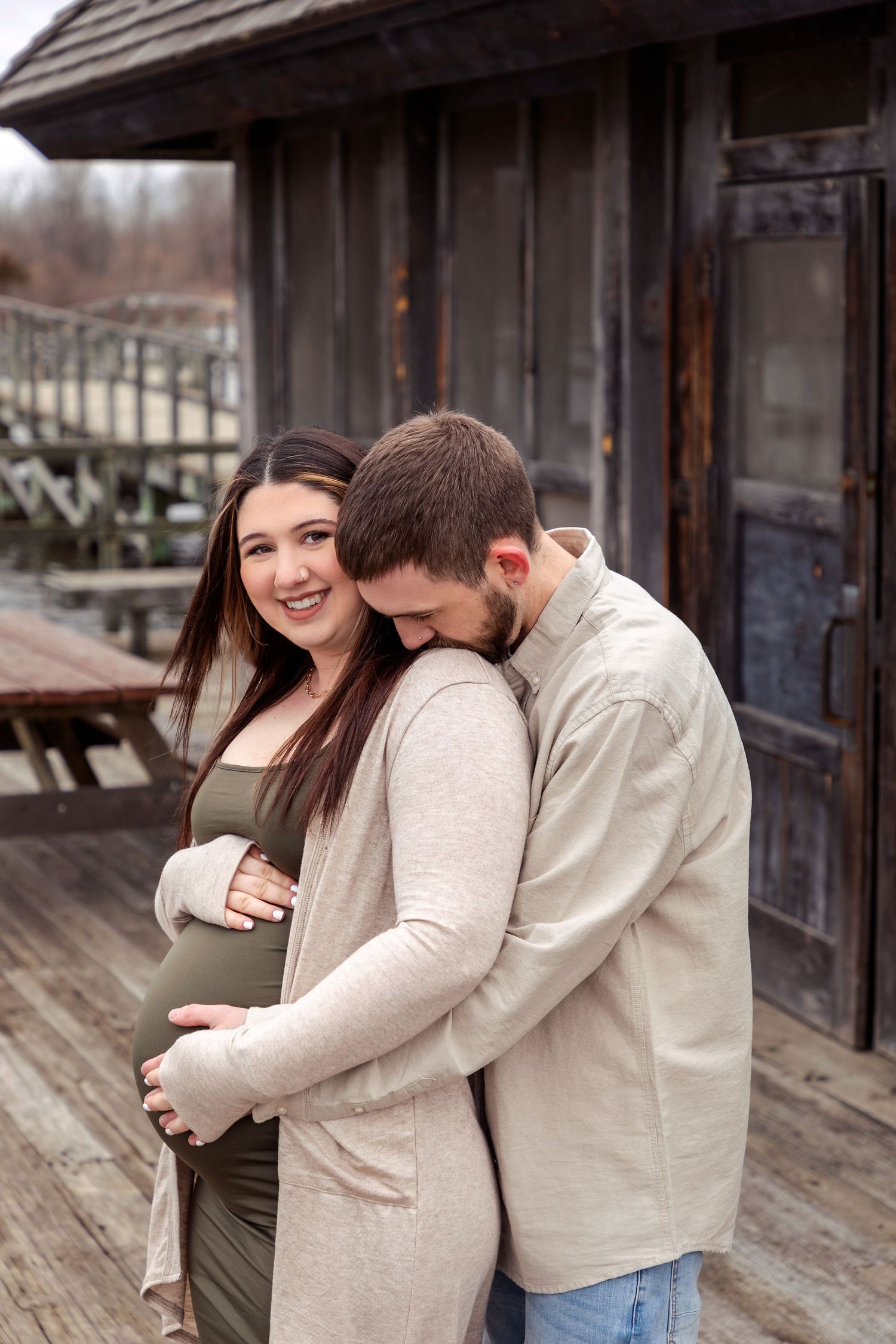 A tender maternity moment captured on a rustic wooden deck outside an old cabin.