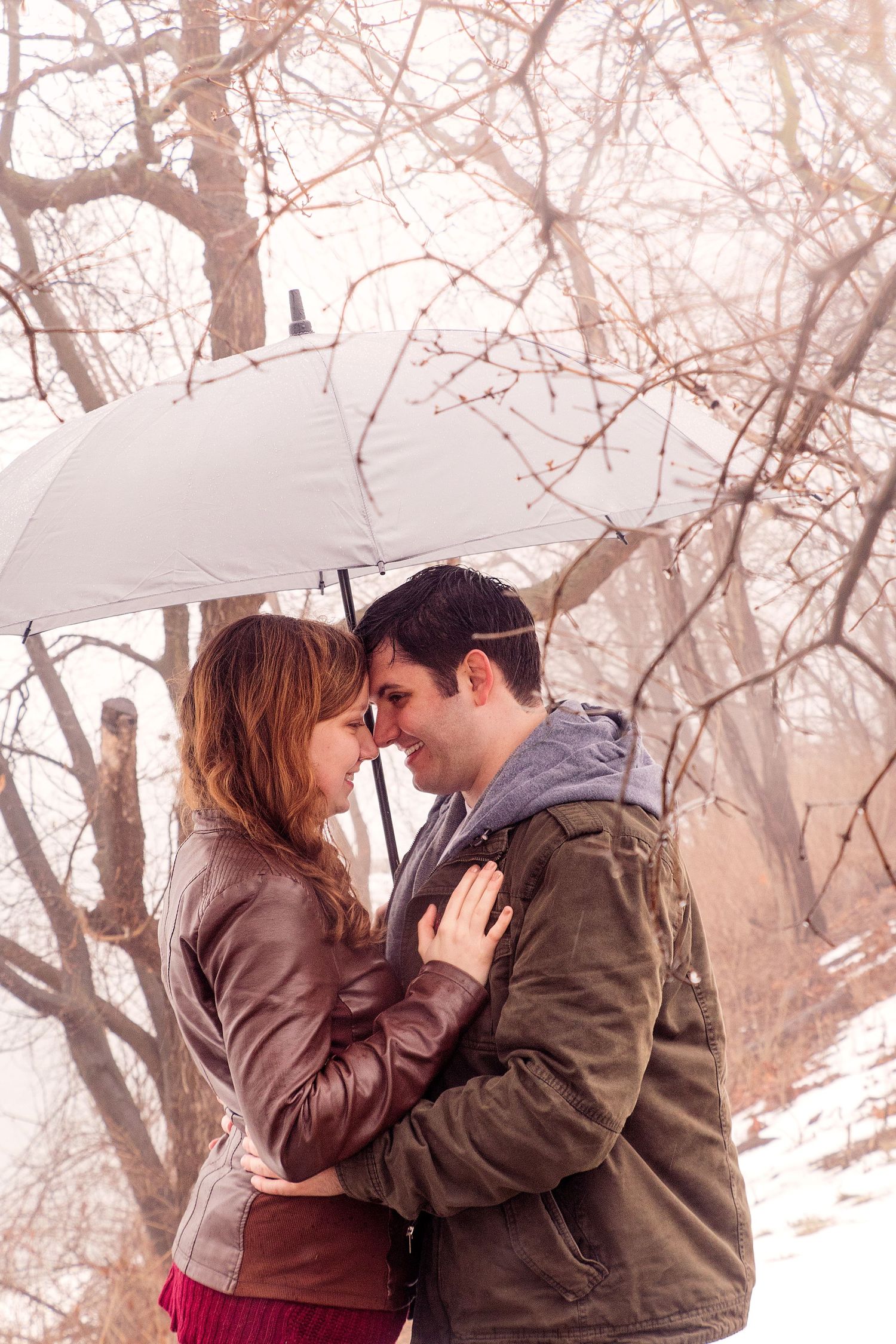 Romantic winter scene with couple sharing intimate moments under white umbrellas in snowy setting.