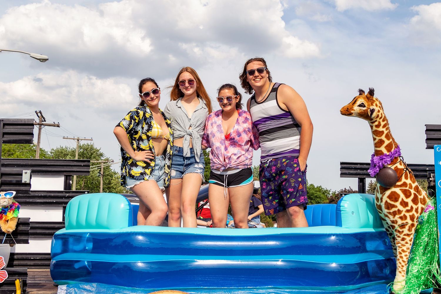 Friends pose together in a blue inflatable pool with summer decorations and a giraffe float.