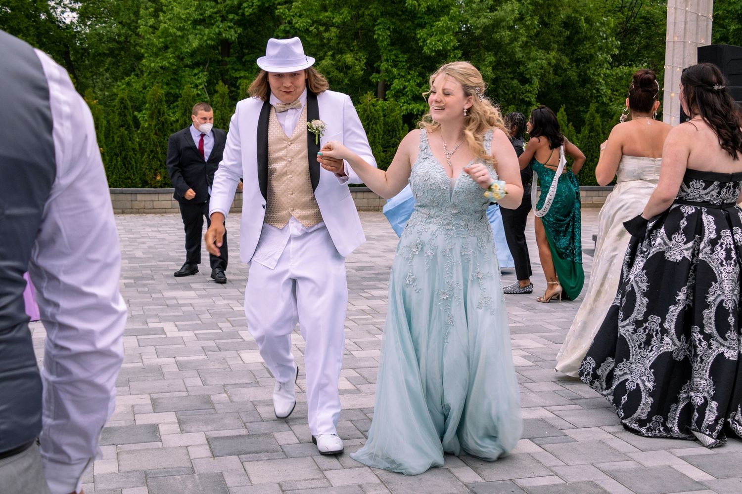 People dance together at an outdoor event wearing formal attire on a stone patio.