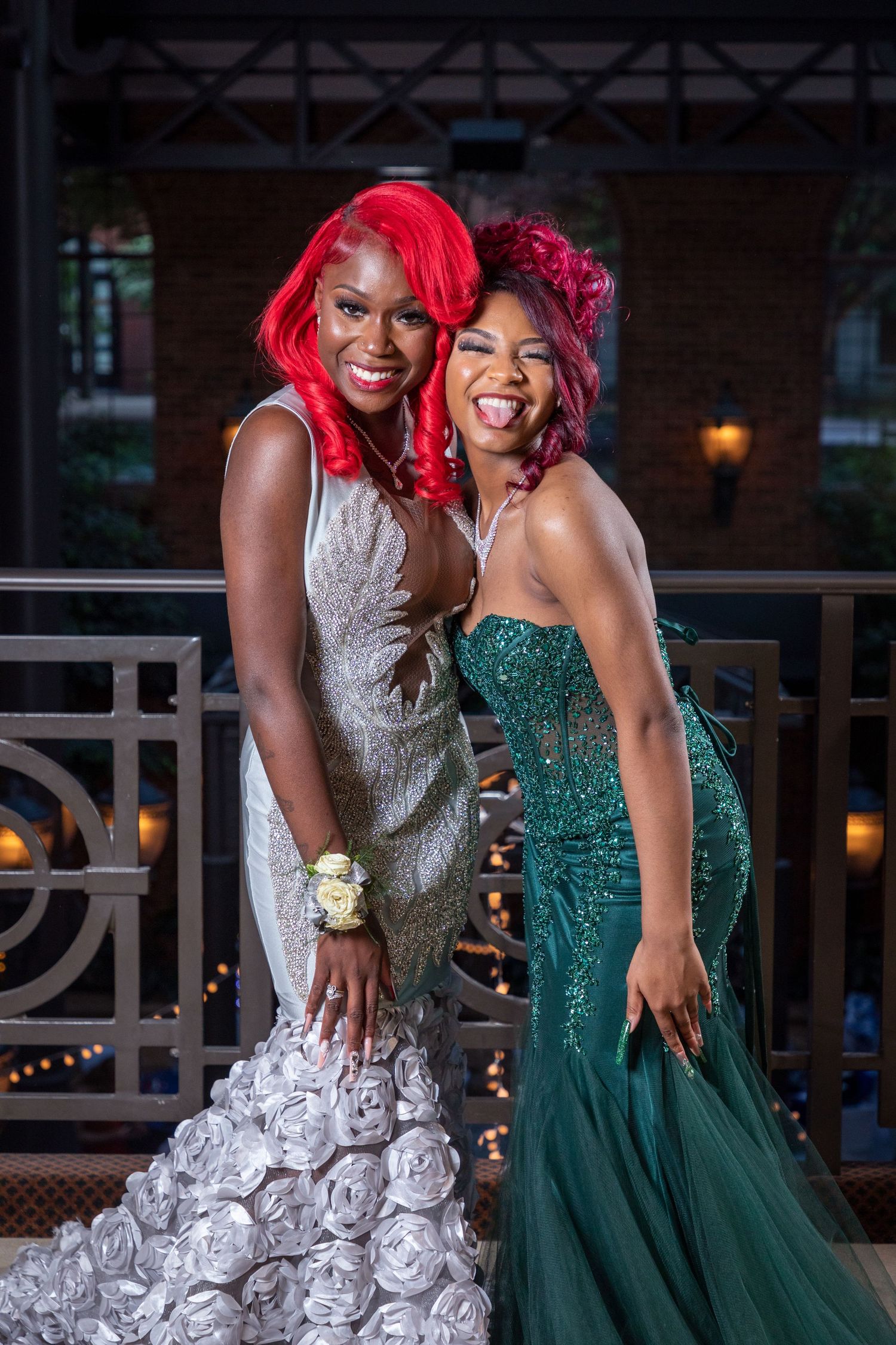 Two friends in elegant gowns, one white and one emerald green, posing together at a formal event.
