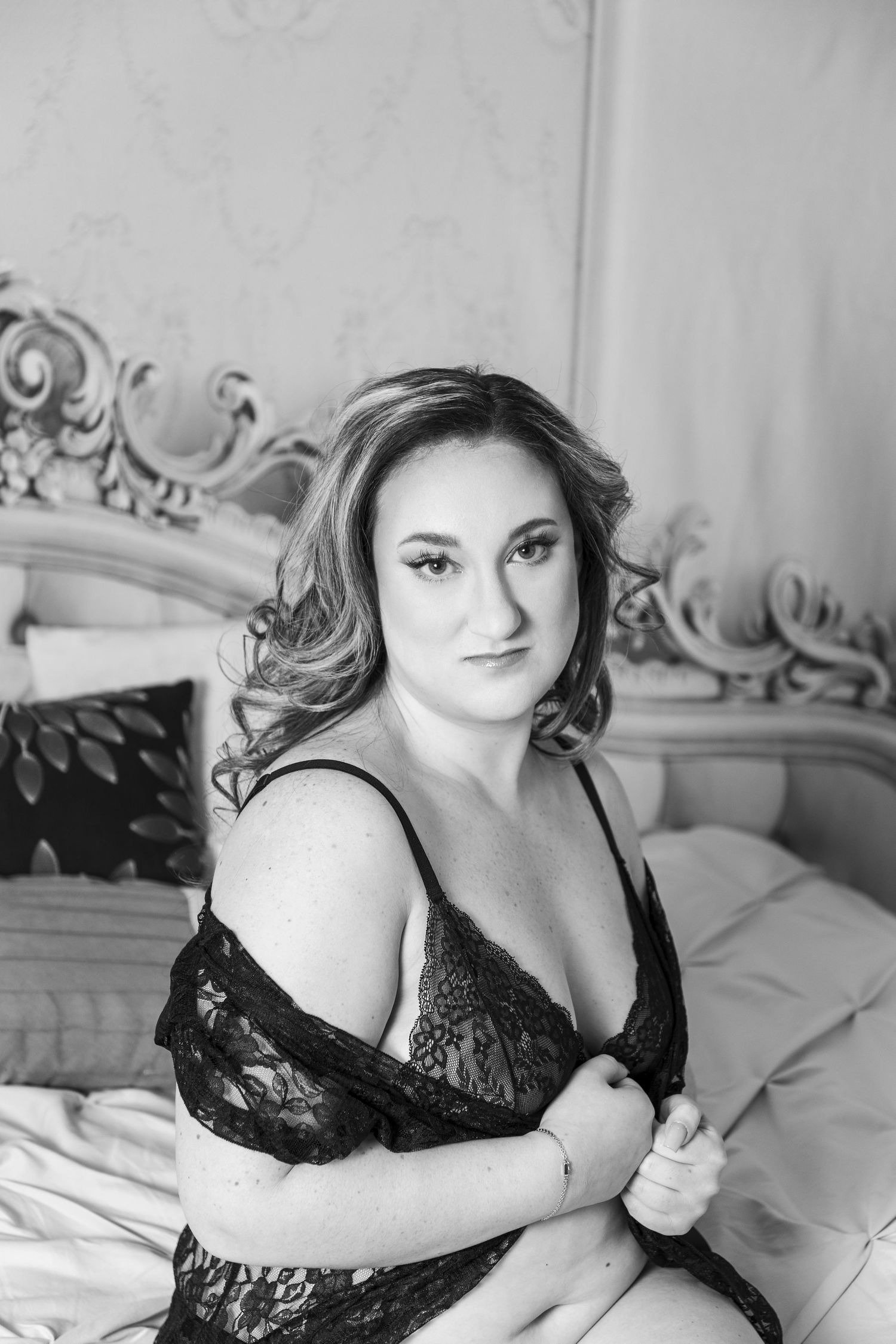 Black and white boudoir portrait with ornate headboard.