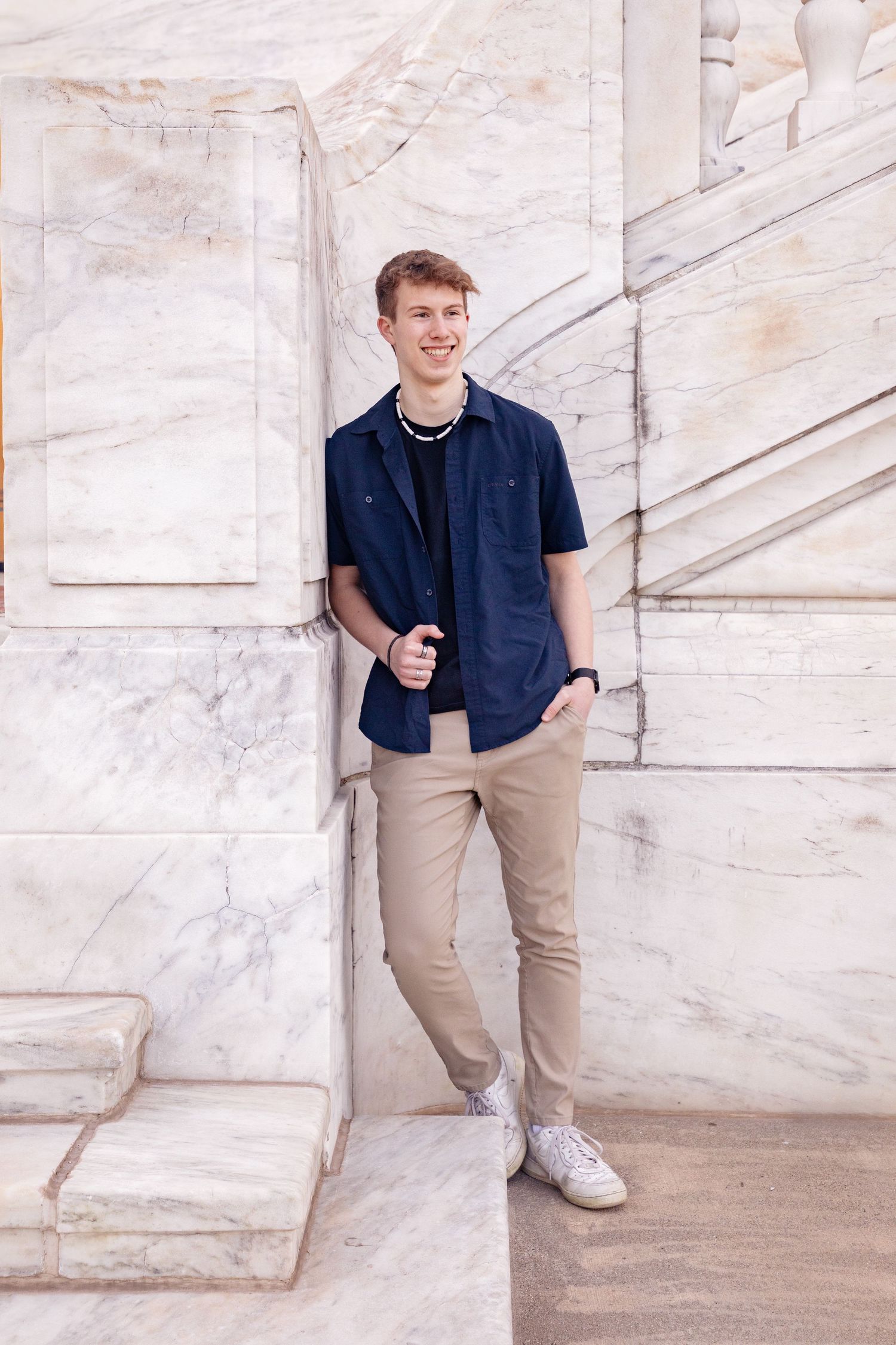 Person in navy polo shirt poses against white marble wall background.