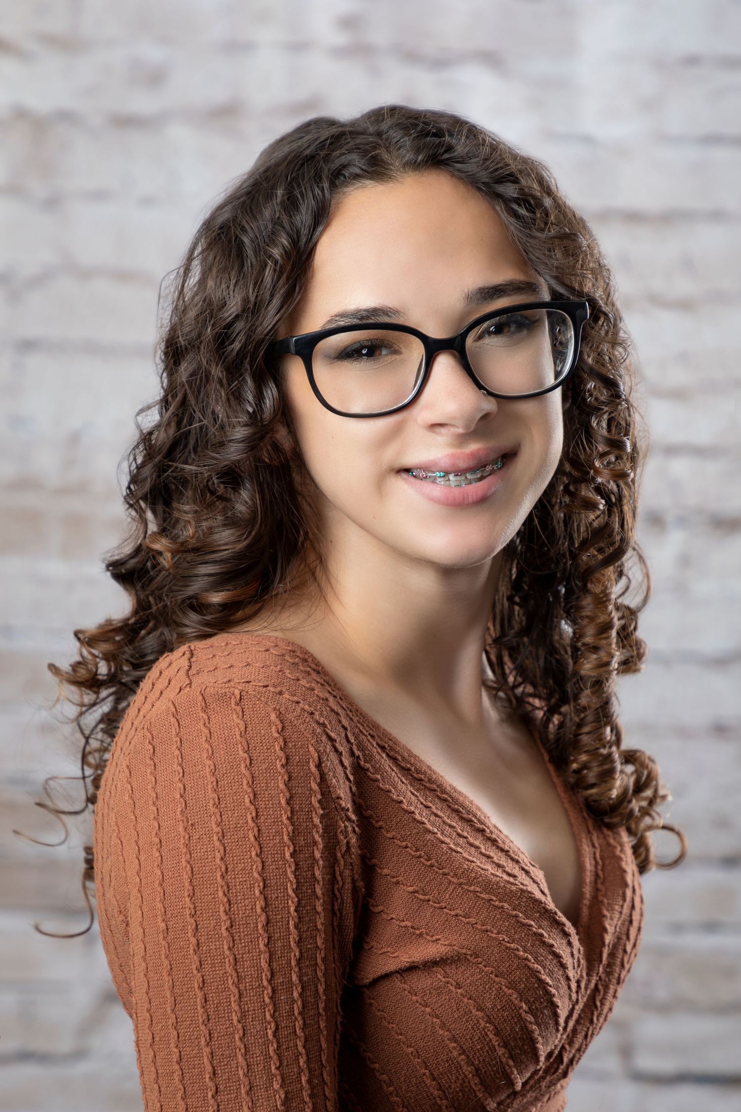 Portrait series showing someone in glasses and brown sweater against brick wall background.