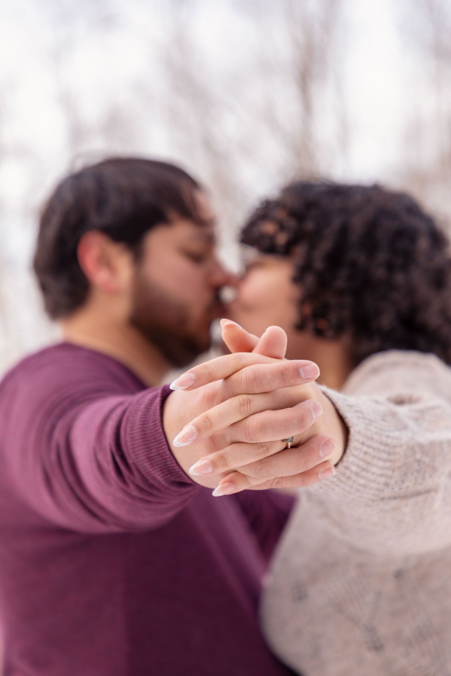 Close-up of clasped hands and intimate embrace against a snowy backdrop.