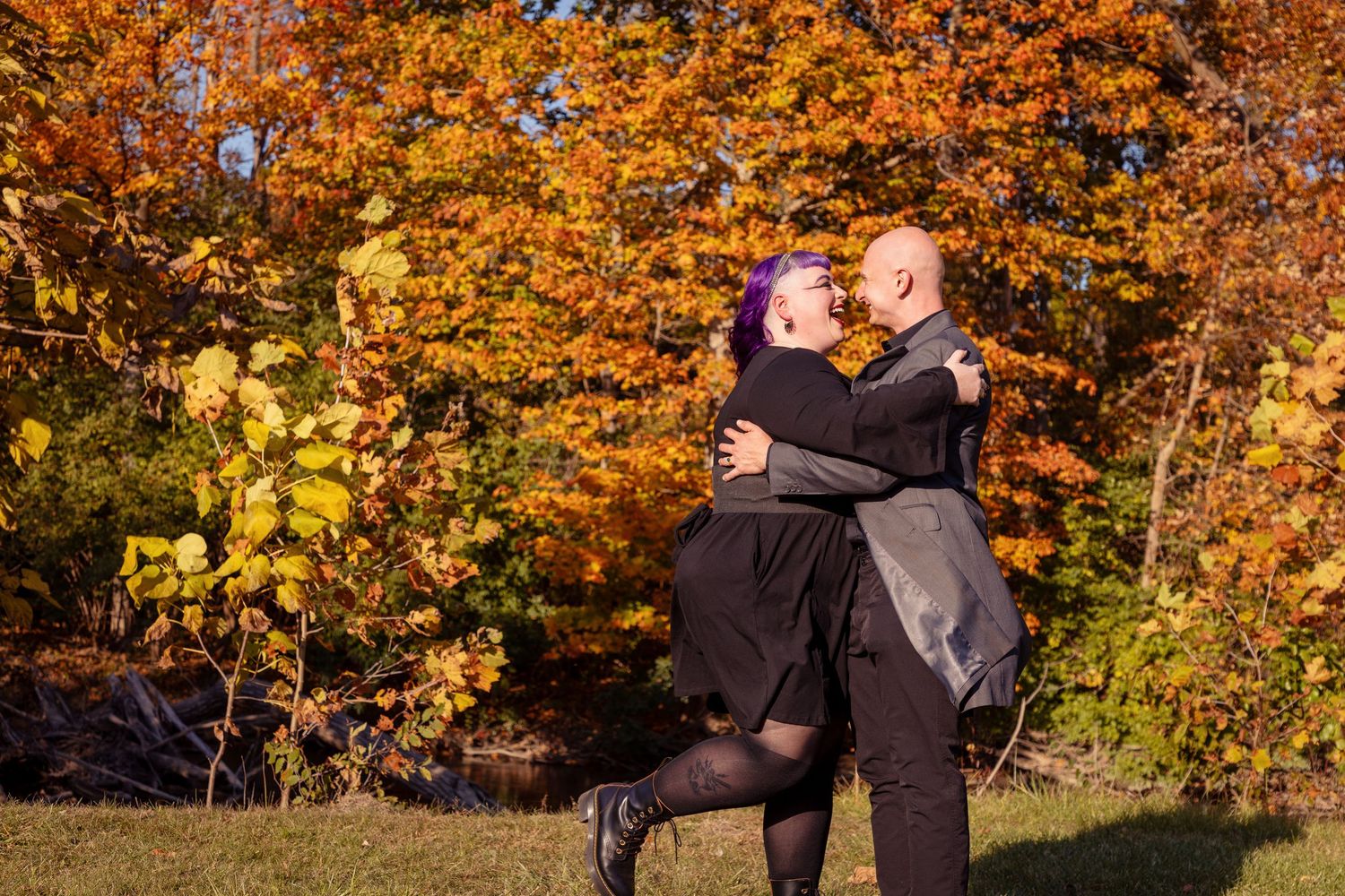 Couple embracing outdoors with vibrant orange fall foliage in the background.
