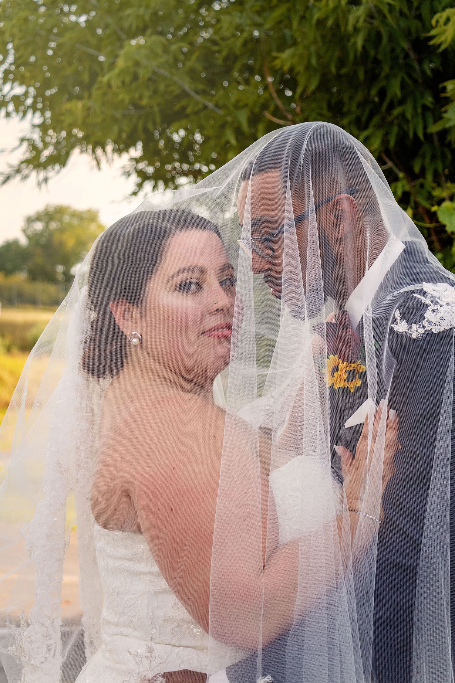 A romantic moment between newlyweds sharing a veil during golden hour.