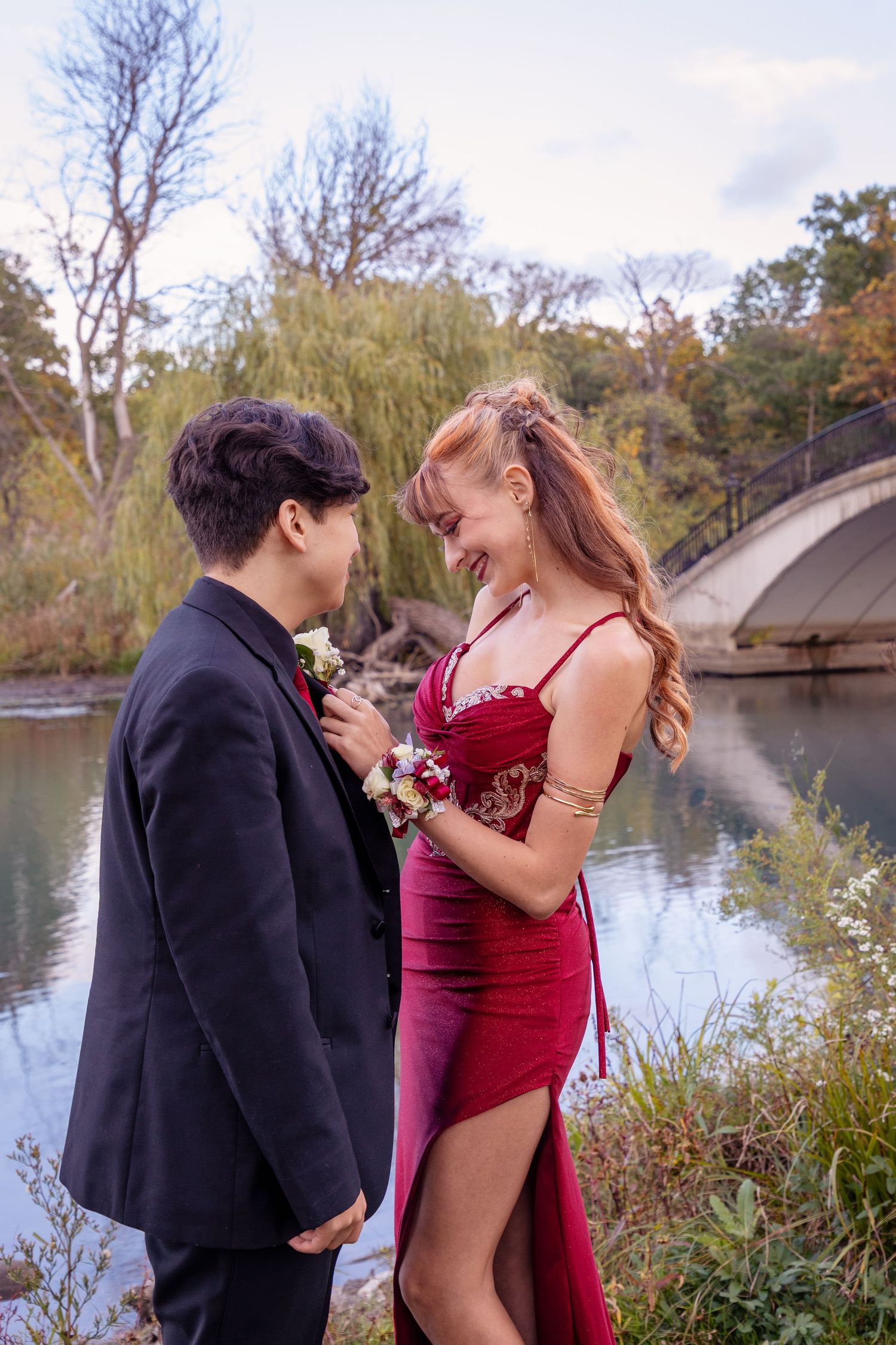 Couple in formal attire sharing romantic moment by lakeside during autumn.