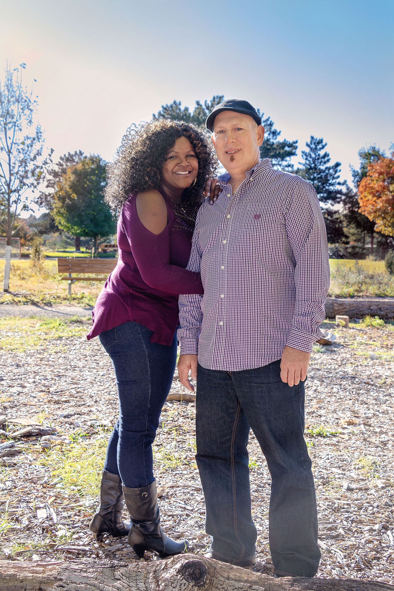 A couple embraces on rocky terrain with autumn trees in the background.