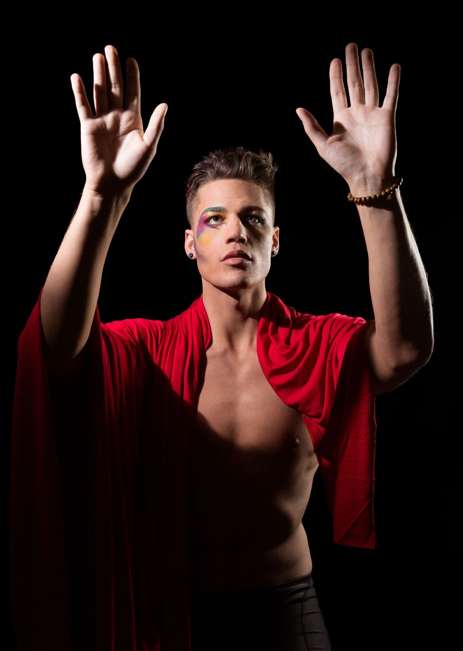 A dramatic portrait with raised hands against a black background in red clothing.