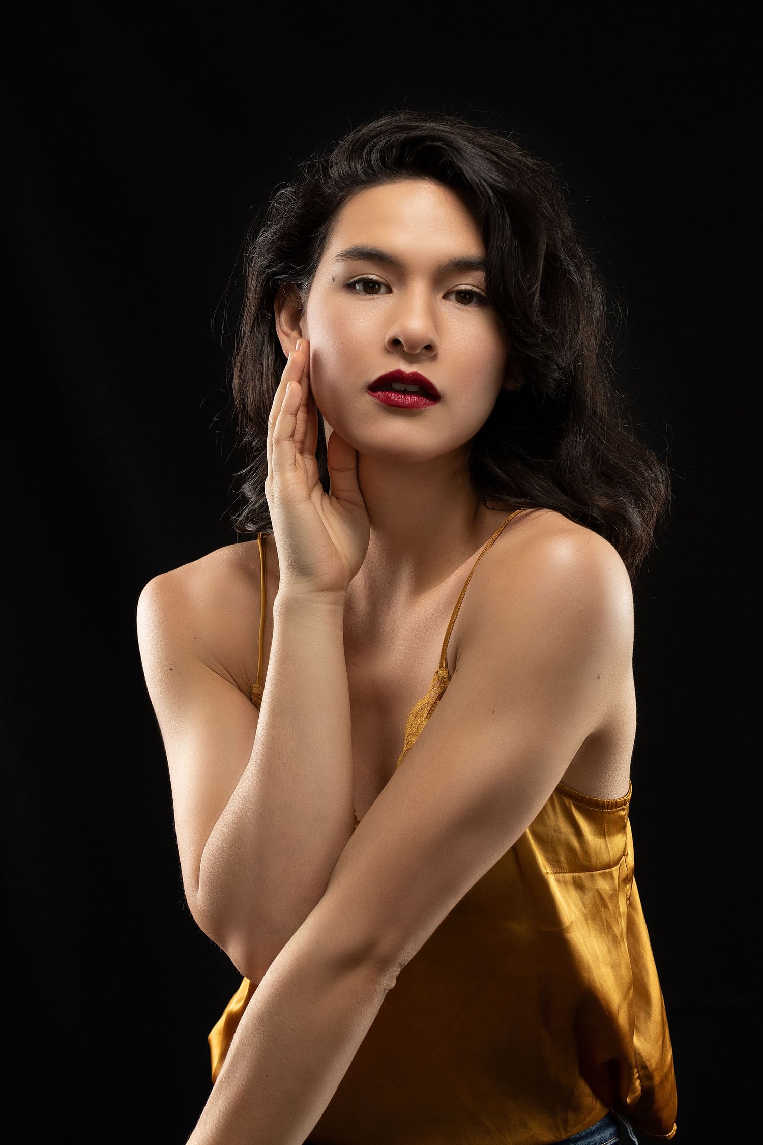 Dramatic portraits against black background wearing gold satin top with bold red lips.