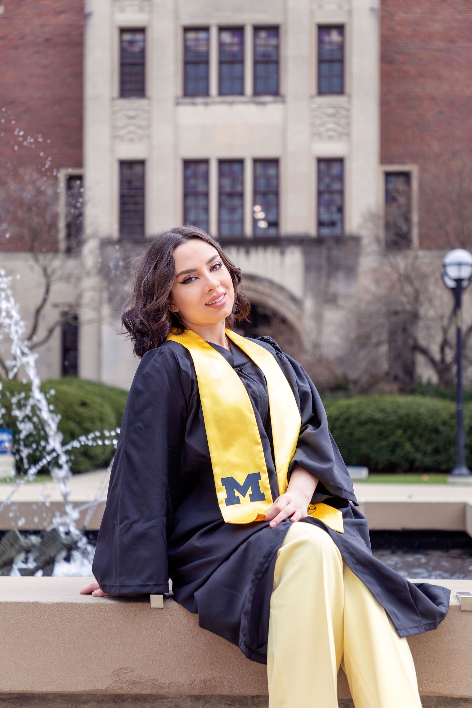 Graduate in yellow and blue university regalia poses on campus.