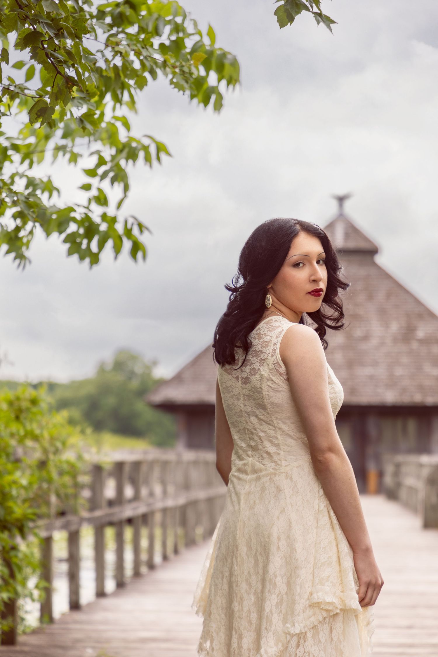 Romantic outdoor photoshoot in cream lace dress against wooden gazebo and green foliage.