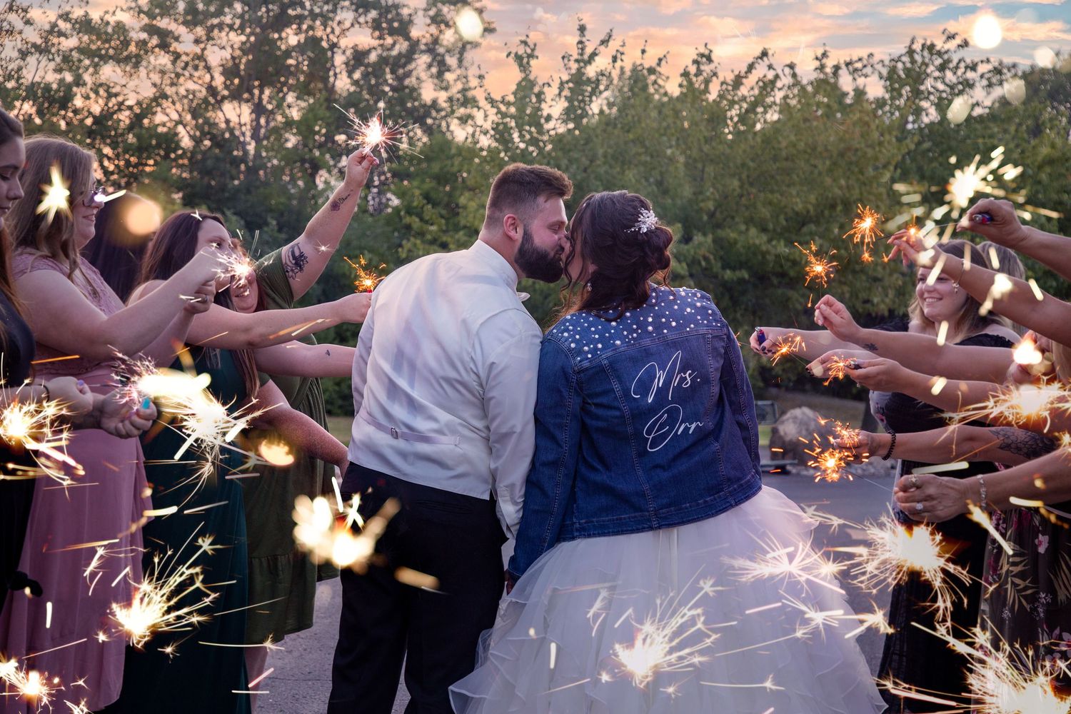 Wedding guests hold sparklers creating magical light trails during evening celebration.