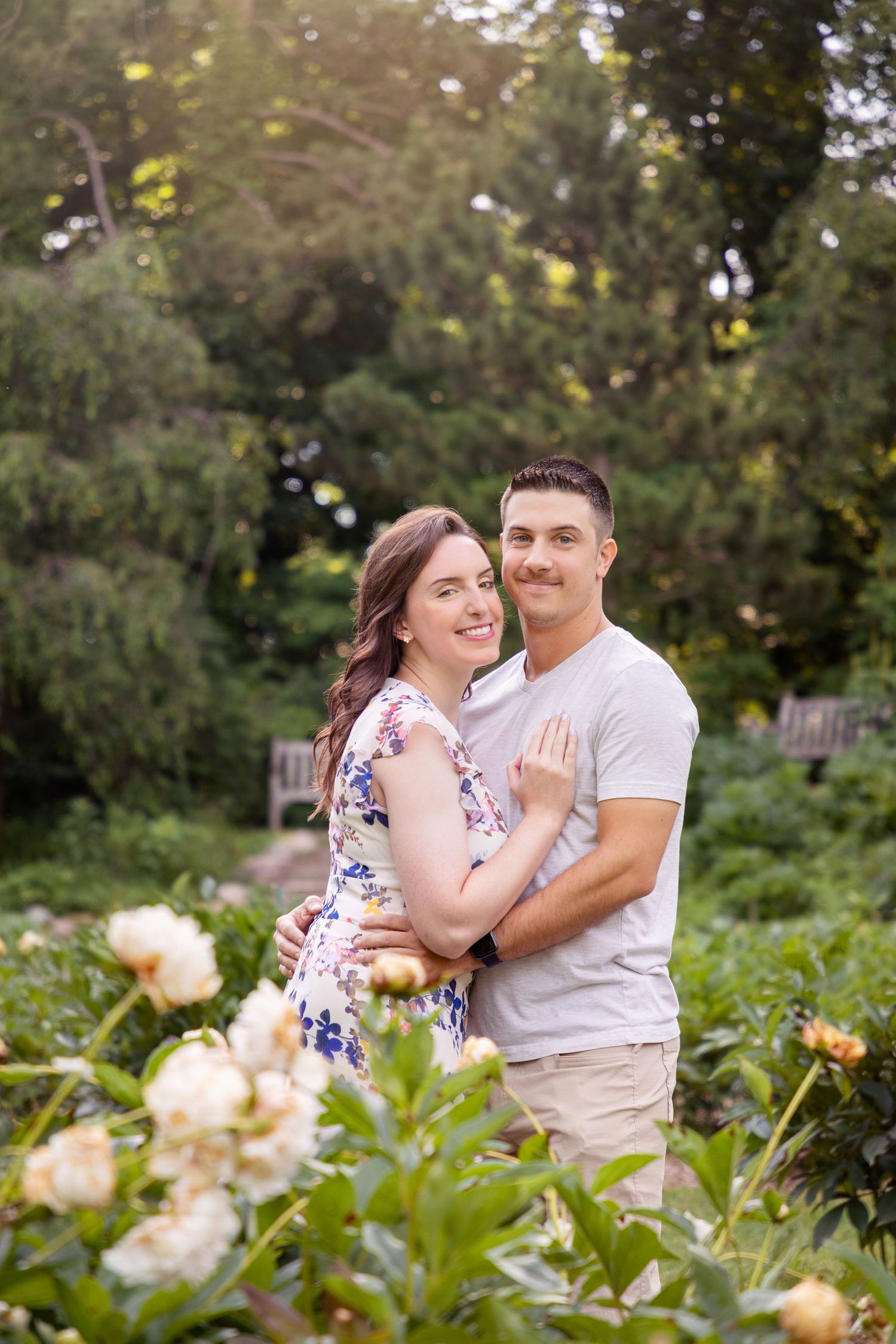 A couple shares playful moments in a garden with blooming flowers.