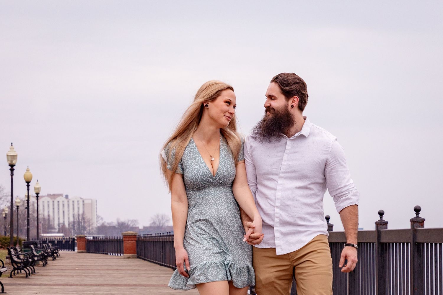 Romantic couple sharing a tender moment together while walking along a city riverfront at sunset.
