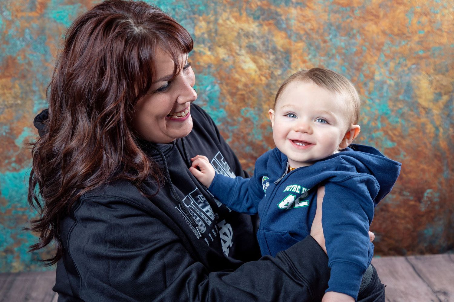 A joyful indoor portrait with a baby in blue against a textured turquoise background.