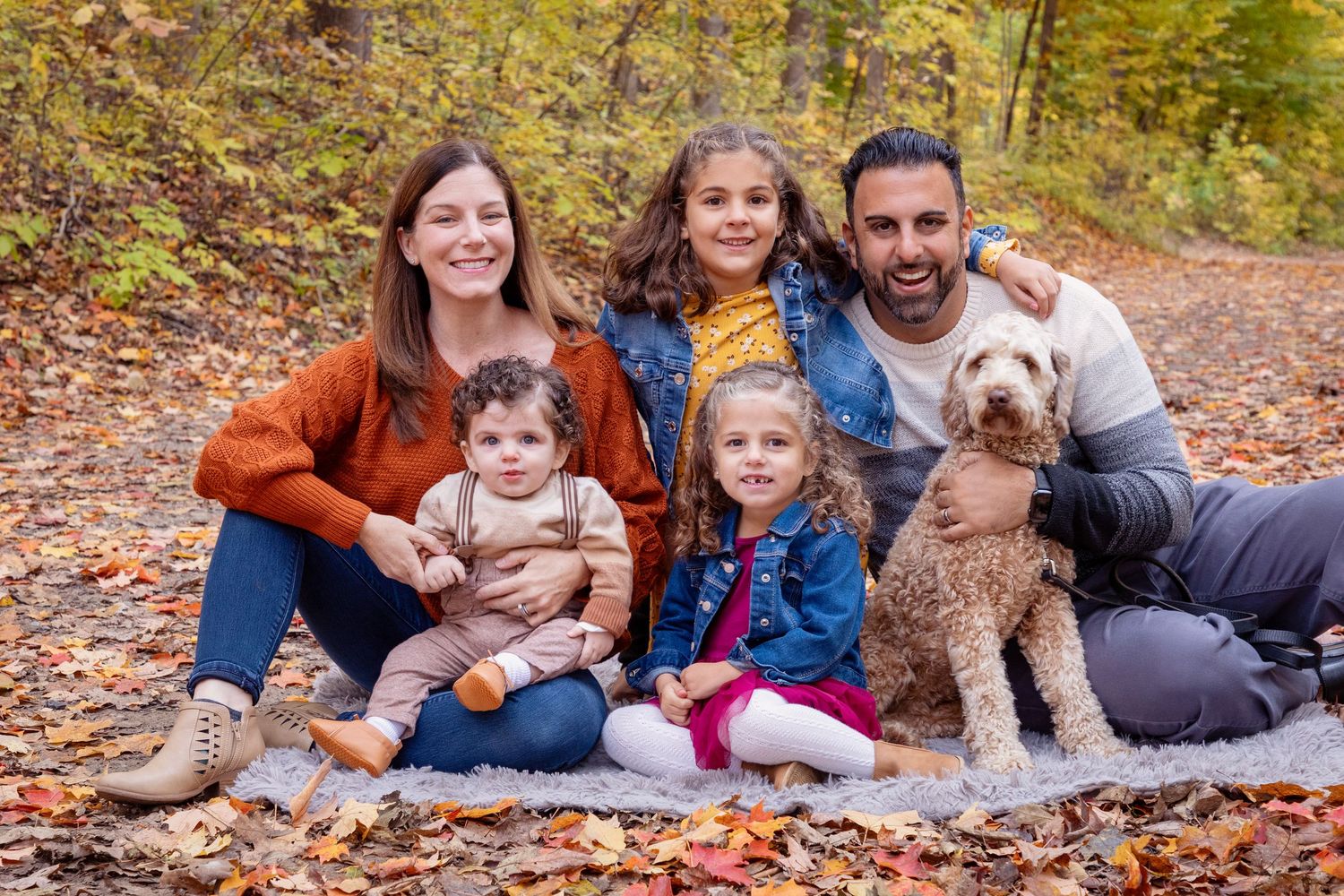 A family and their dog posing together on autumn leaves in an outdoor setting.