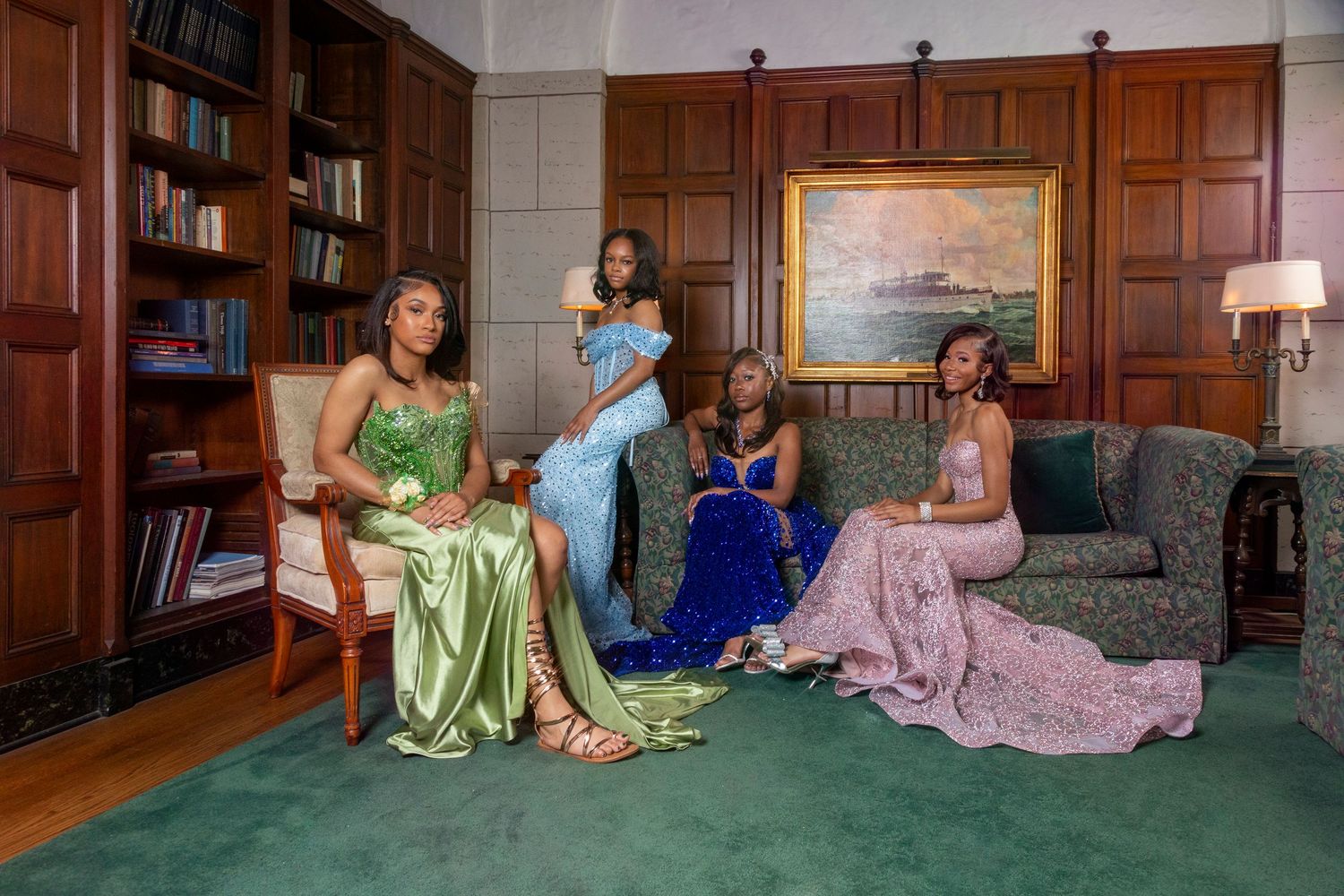 Women in elegant gowns pose together in a luxurious wood-paneled library setting.