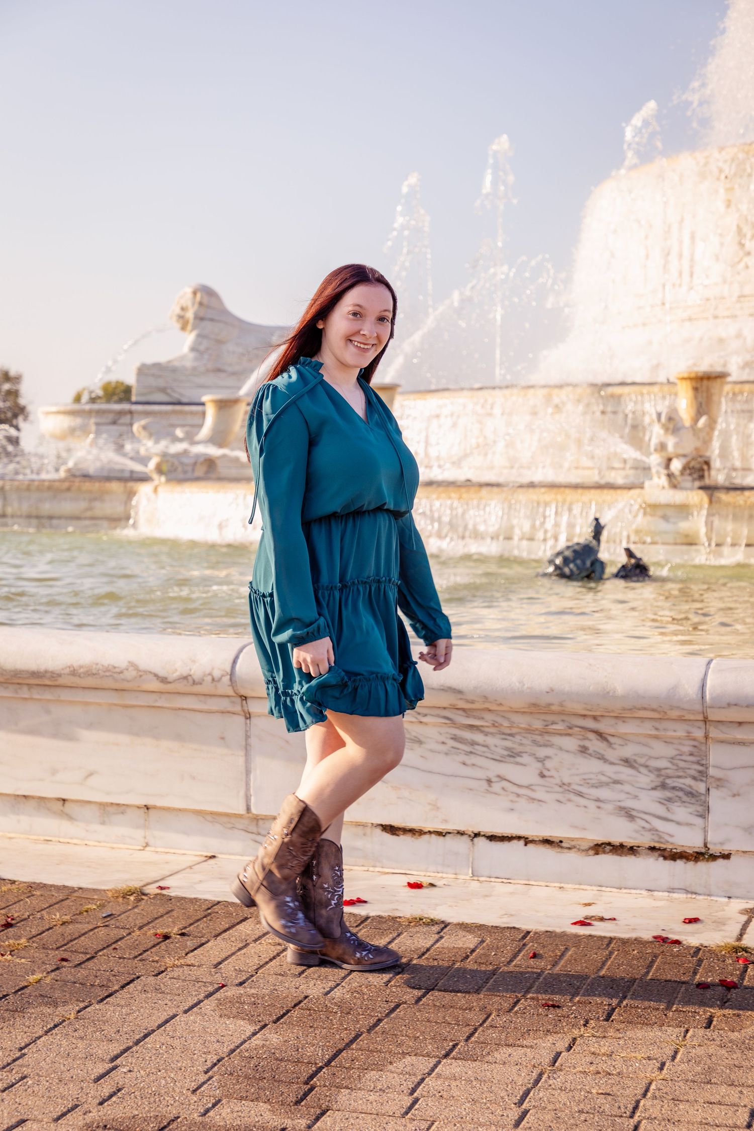 Person in teal dress dances near fountain at sunset.
