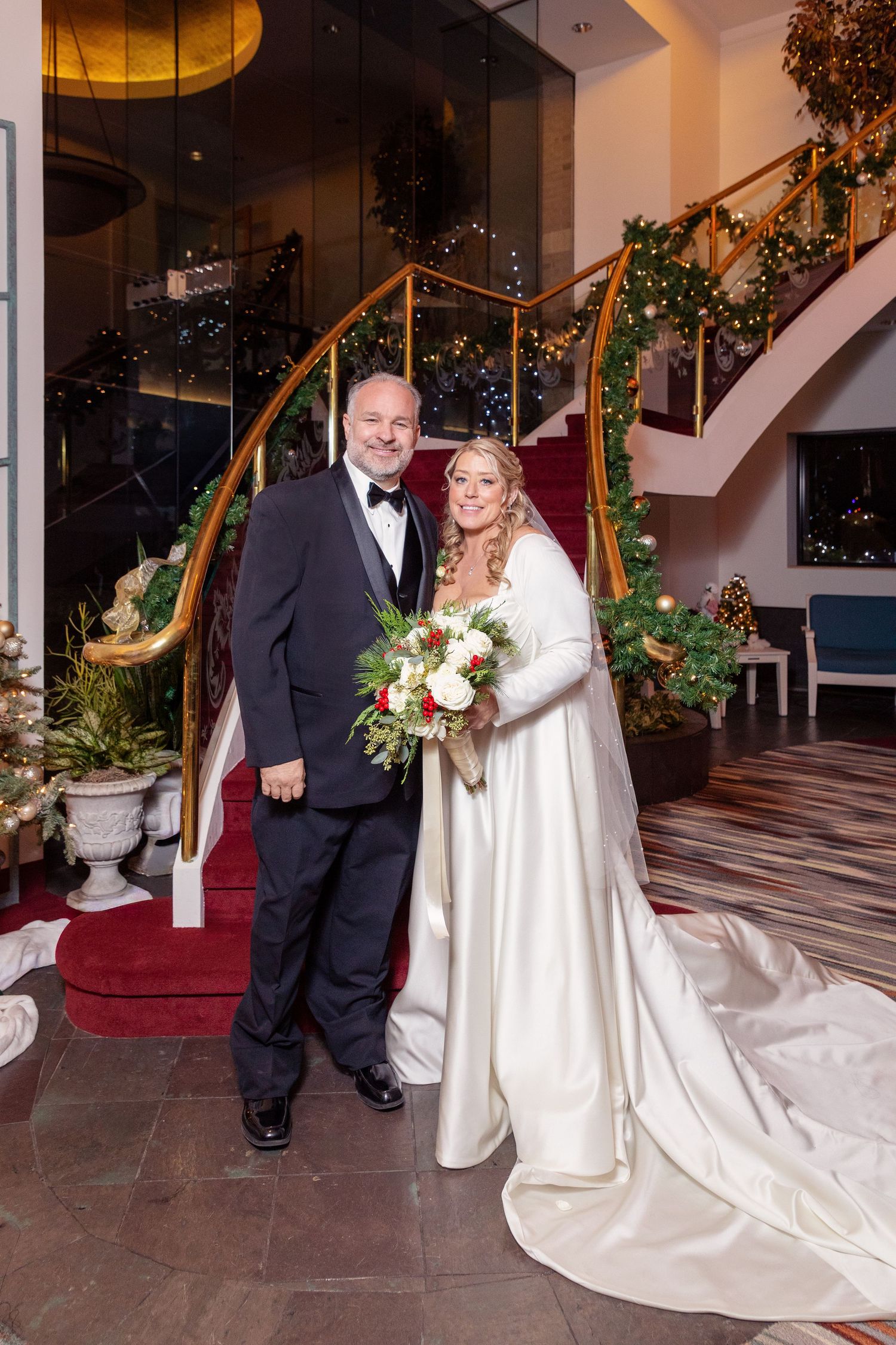 Elegant wedding photos in a grand hotel lobby with decorated staircase and holiday greenery.