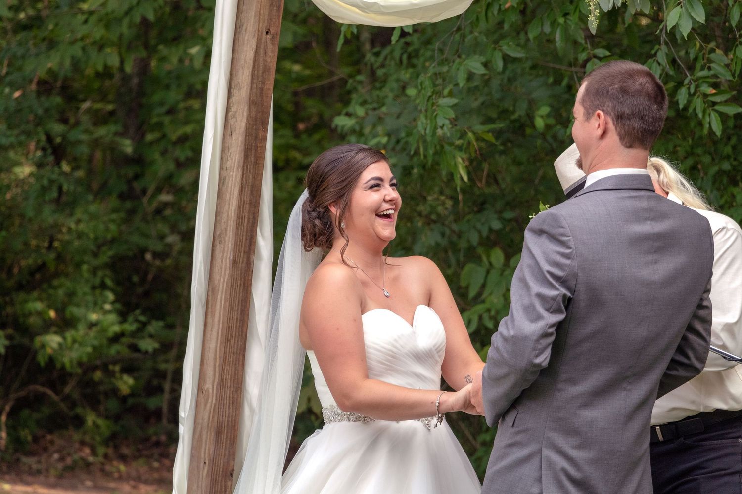 Candid wedding moments captured outdoors with white draped ceremony arch.