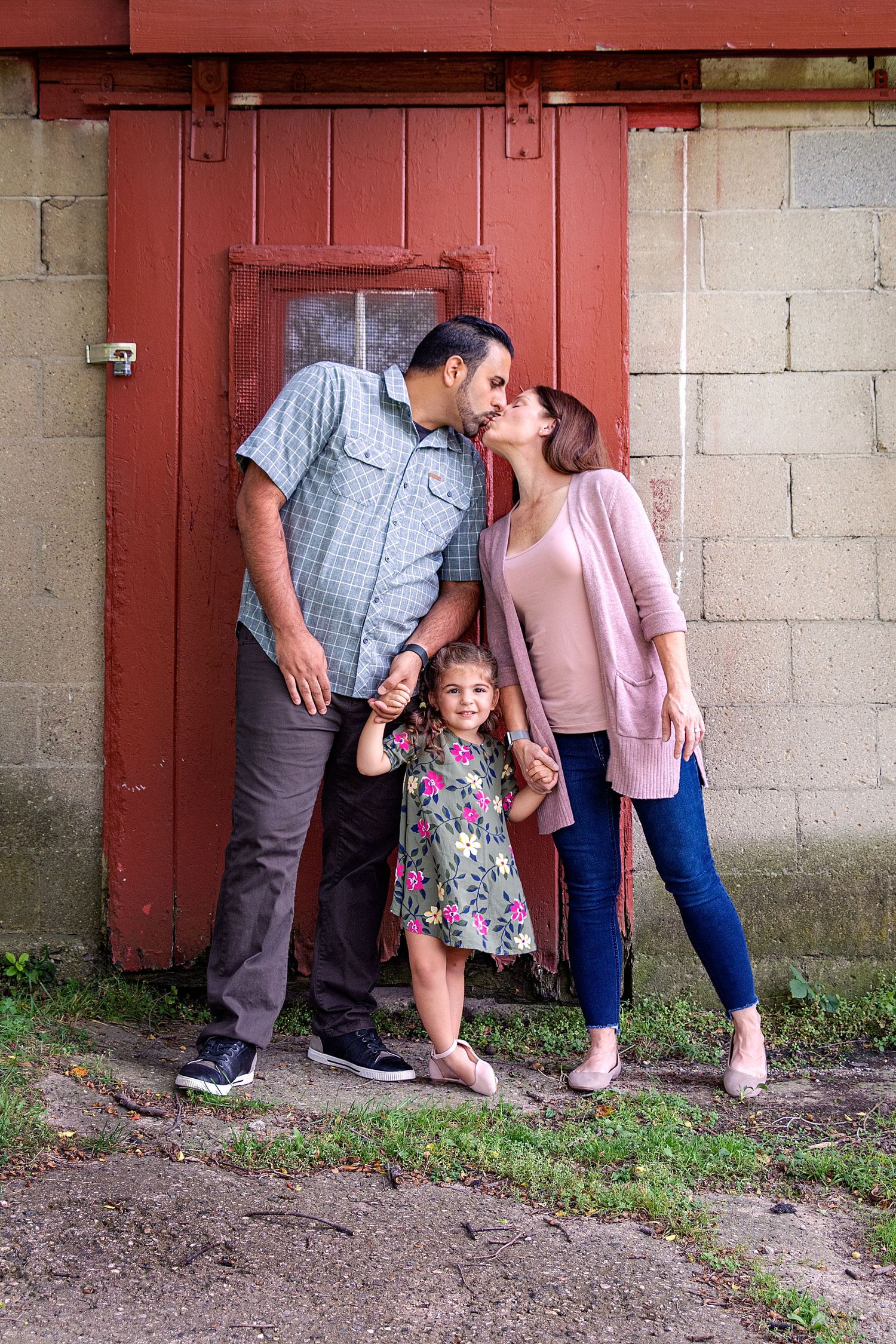 Family portrait session against red barn wall with playful poses and interactions.