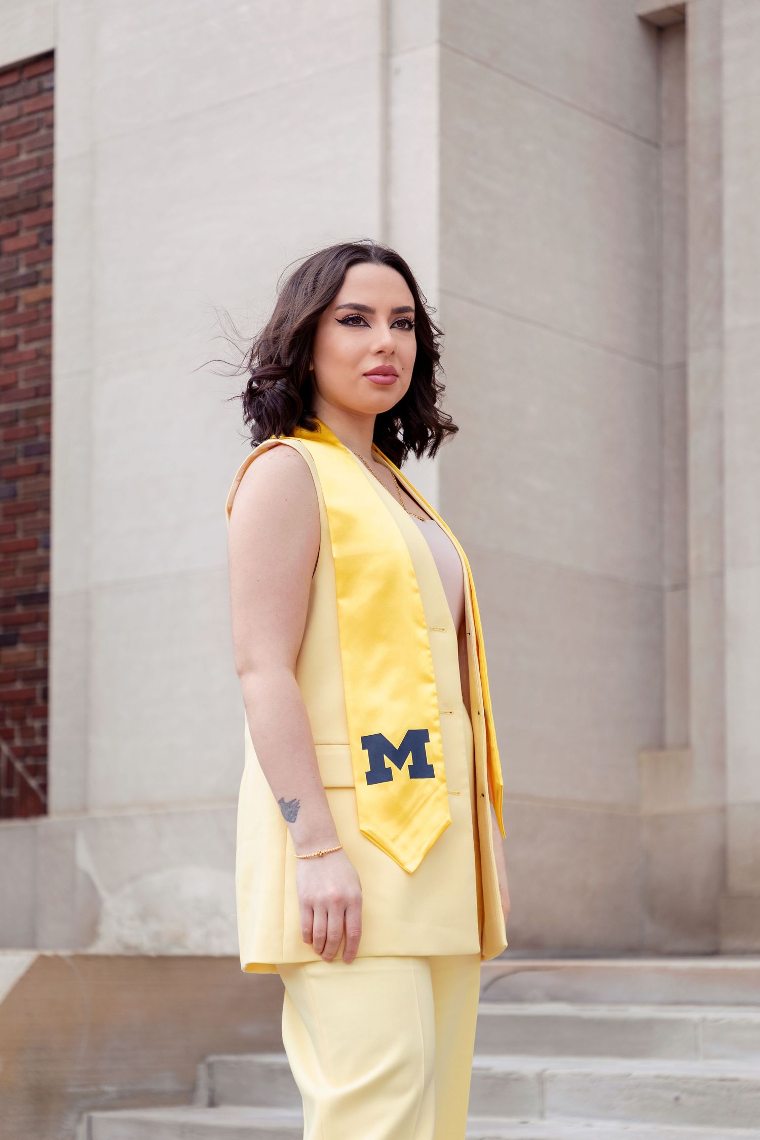 Person in yellow graduation gown poses in front of university building.