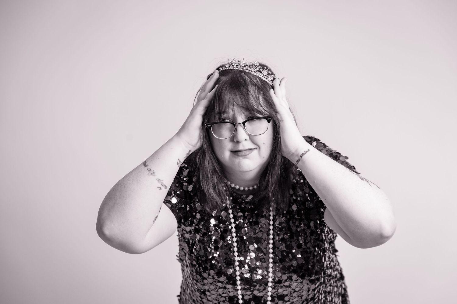A black and white portrait of someone in sequins with hands on head expressing joy.