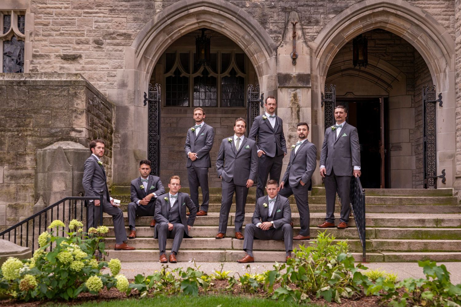 Wedding party posing on stone church steps with Gothic architecture in the background.