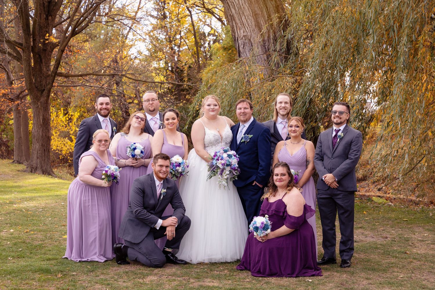 Wedding party poses under autumn trees with golden leaves in the background.