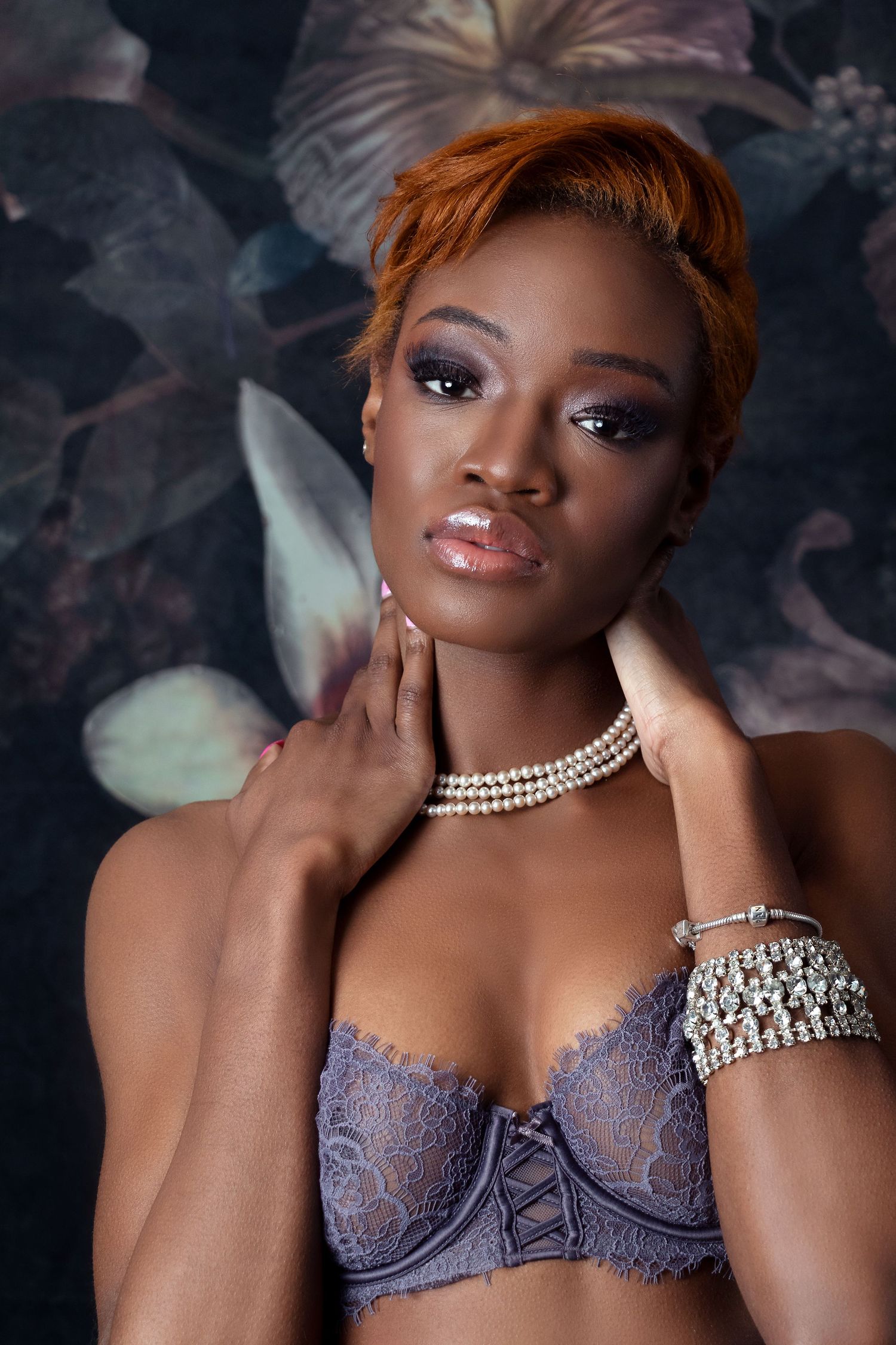 Elegant portrait with pearl necklace and lace lingerie against floral background.
