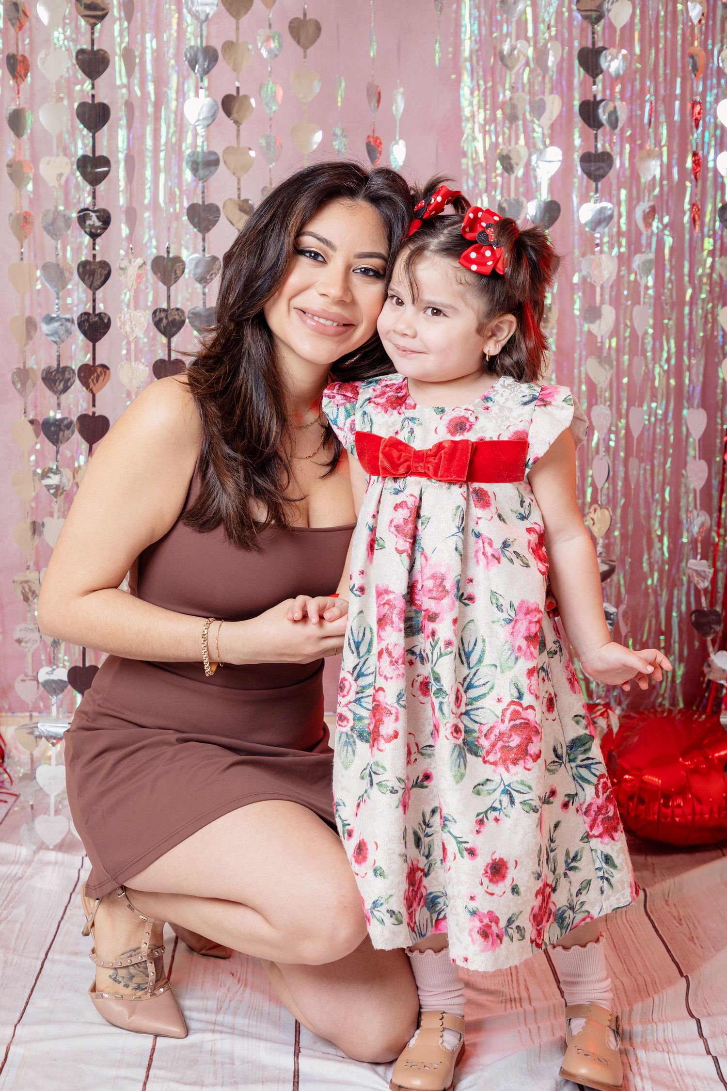 Mother and daughter valentine's day photoshoot with floral dress and pink decorative backdrop.