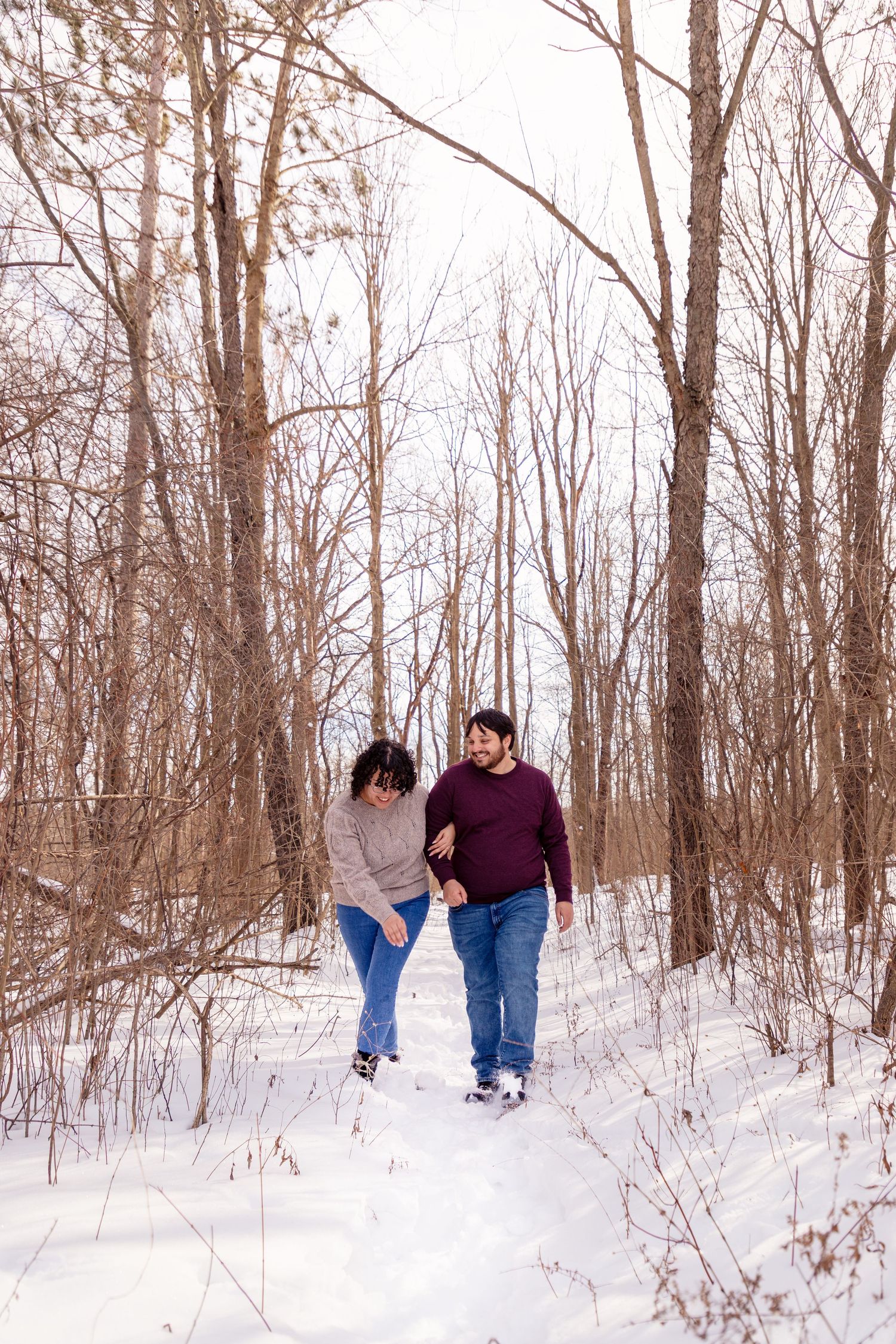 Couple walking hand in hand through a snowy forest path on a winter day.