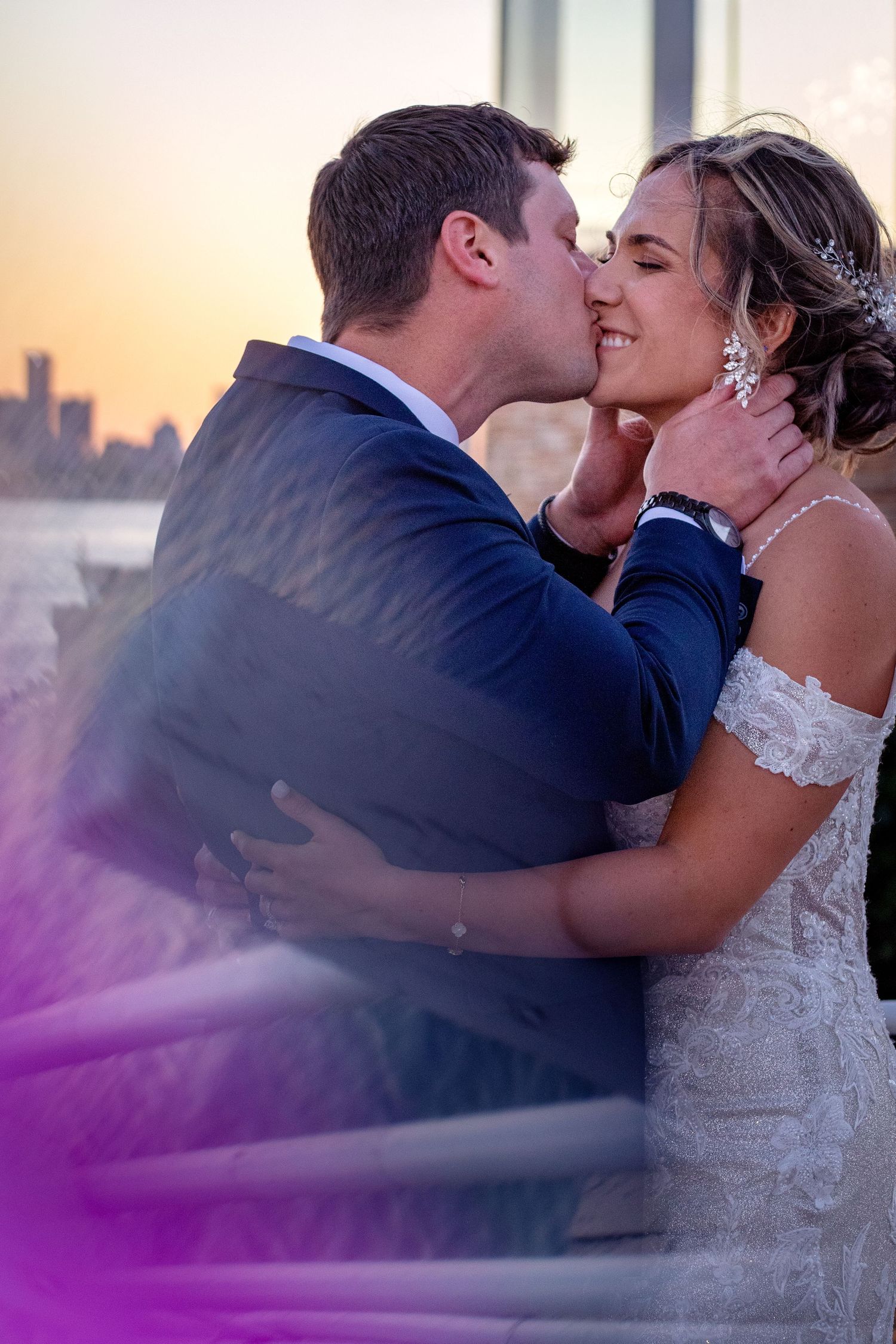Romantic sunset wedding portrait with city skyline visible in background.