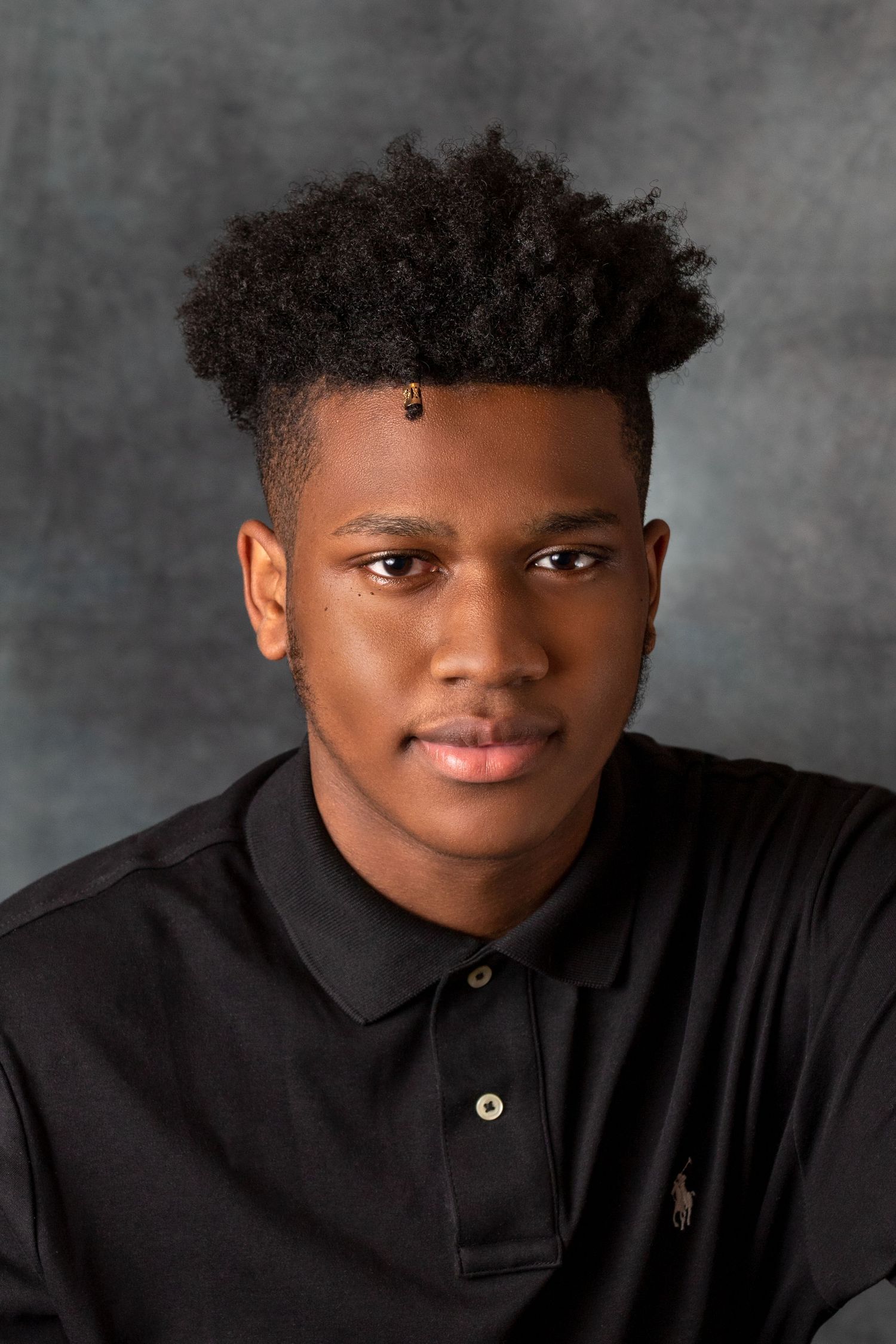 Professional headshots in black polo shirt against grey studio backdrop.