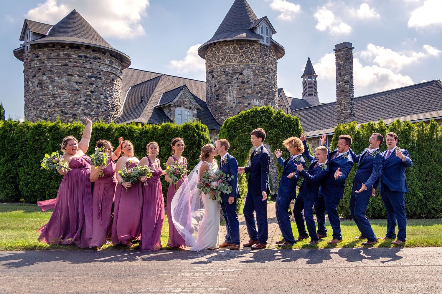 Wedding party in navy and purple attire posed in front of a stone castle building.