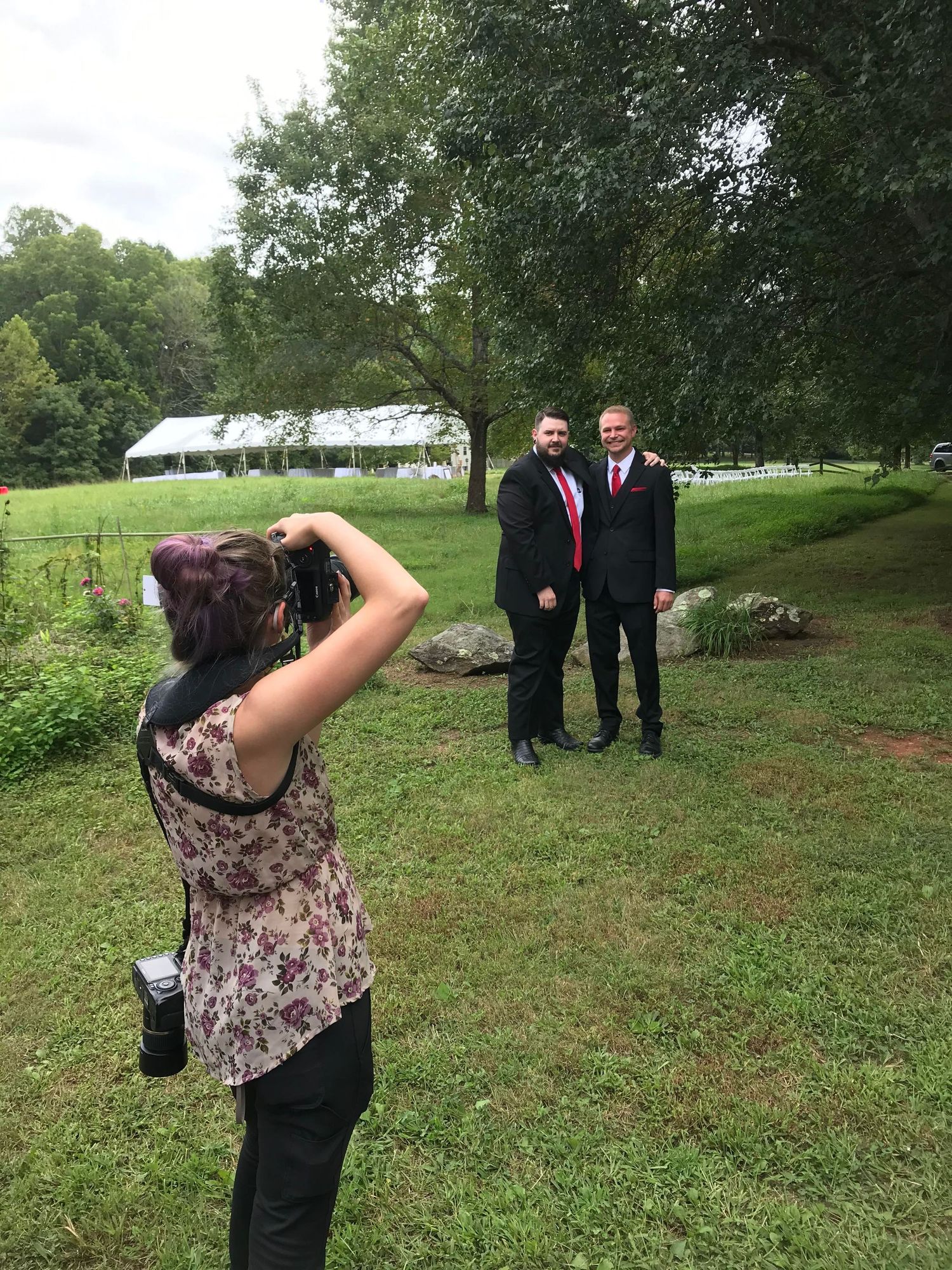 Photographer taking pictures outdoors with suited figures in background.