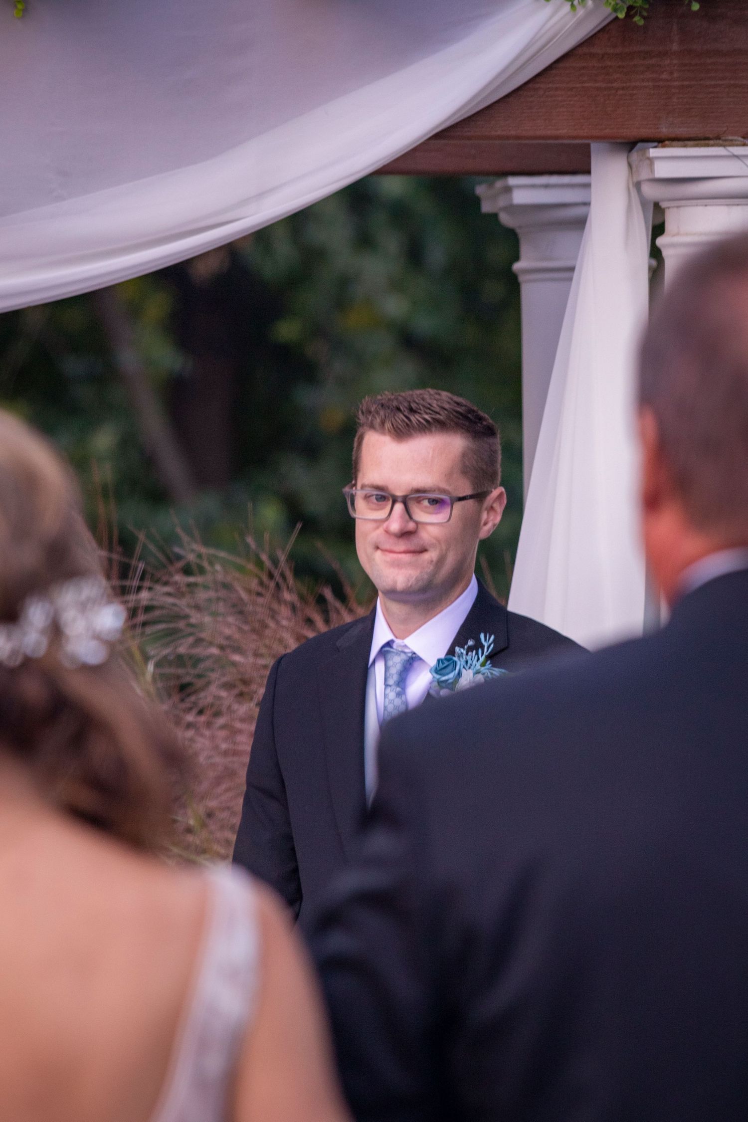 Wedding ceremony moment under white draped pergola with floral decorations.